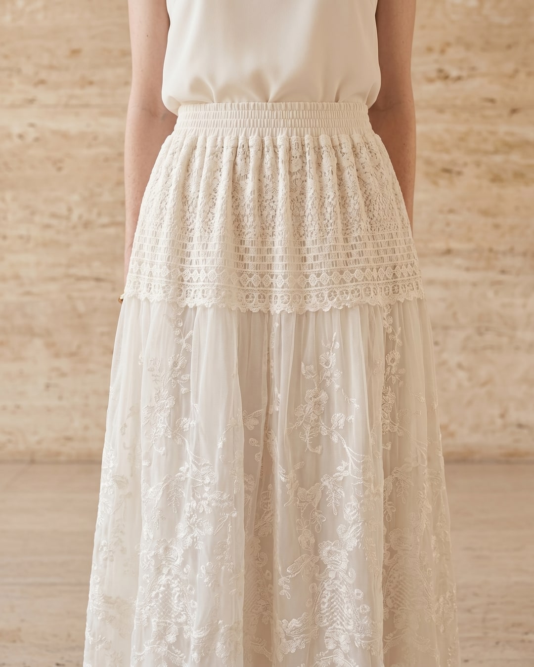 Aemilia dress in Avorio — three-quarter view showing the shirred elastic waist, scoop neckline and tonal floral lace embroidery in a Hugo Caesar Tassi travertine studio