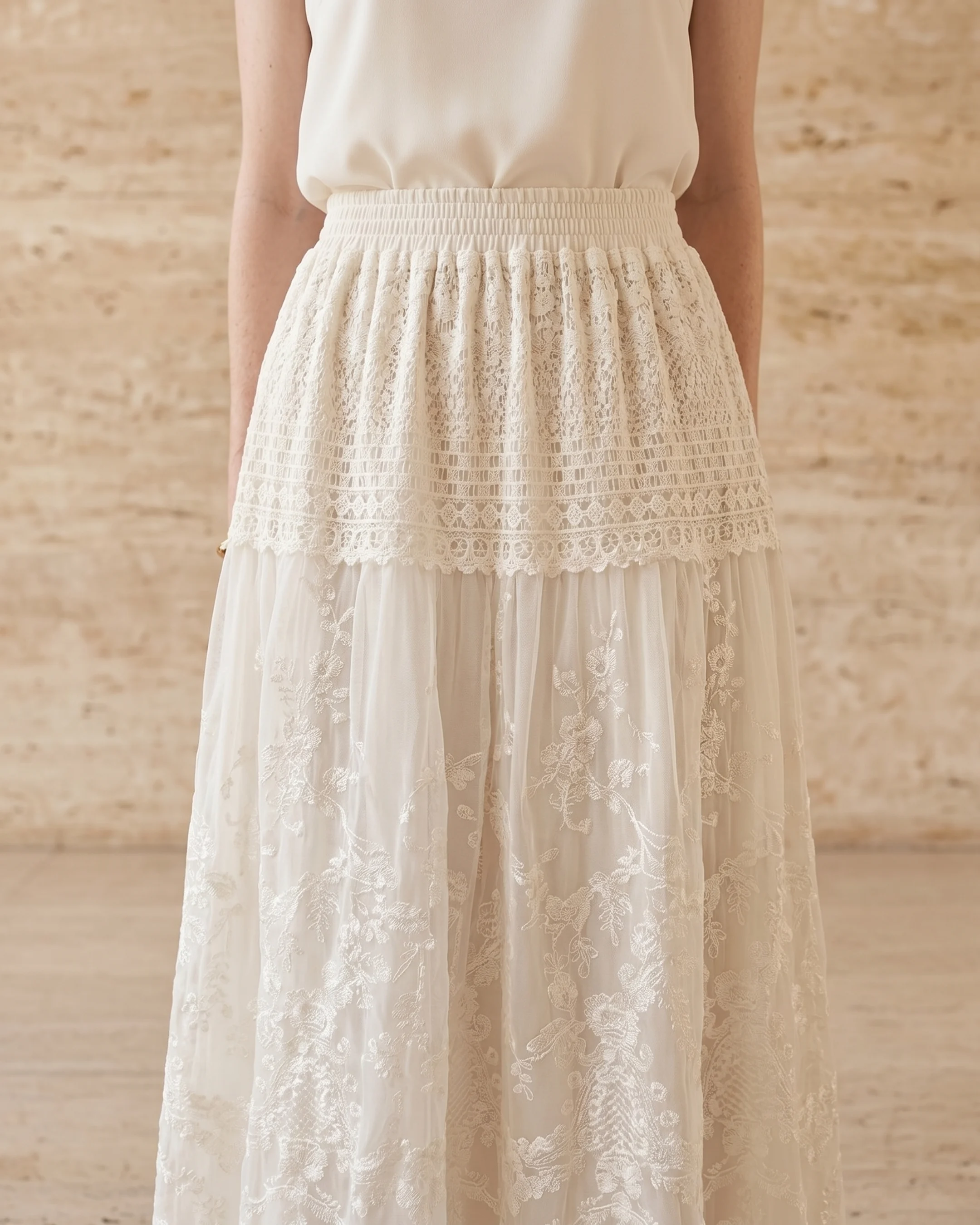Aemilia dress in Avorio — three-quarter view showing the shirred elastic waist, scoop neckline and tonal floral lace embroidery in a Hugo Caesar Tassi travertine studio