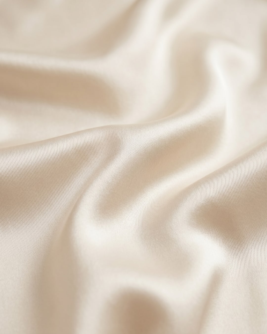 Macro detail of the Hugo Caesar Tassi Calpurnia champagne liquid-satin fabric, showing its lustrous bias-cut drape on travertine stone