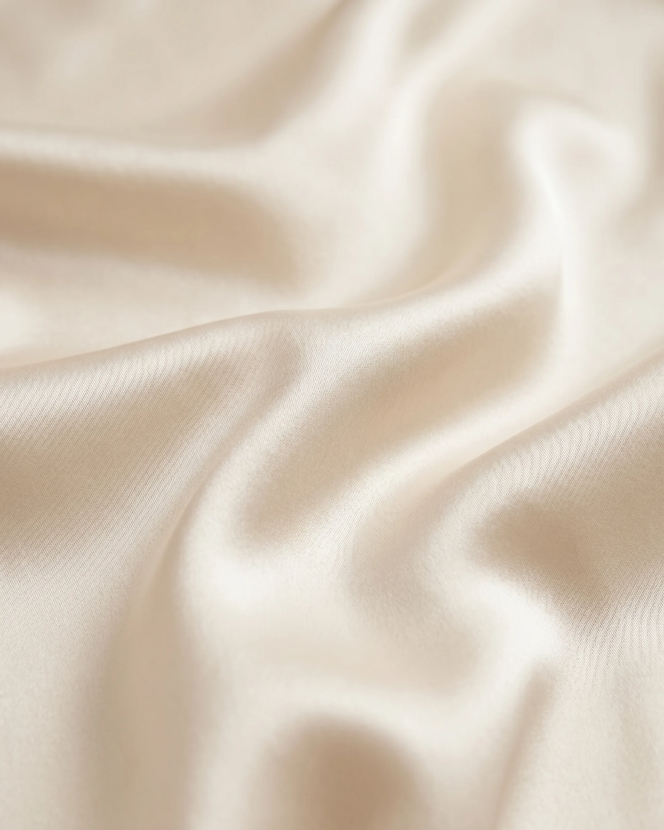 Macro detail of the Hugo Caesar Tassi Calpurnia champagne liquid-satin fabric, showing its lustrous bias-cut drape on travertine stone