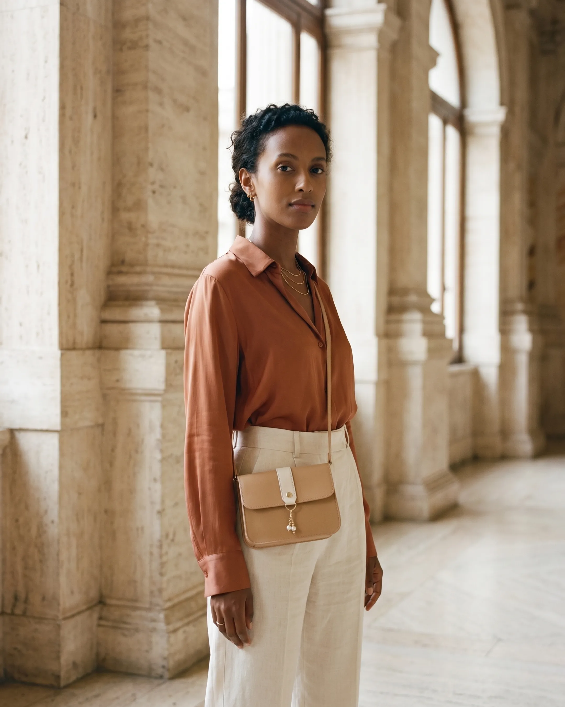 Model wearing the Hugo Caesar Tassi Capitolina color-block leather crossbody bag in Travertine across the body in a sunlit Roman travertine colonnade