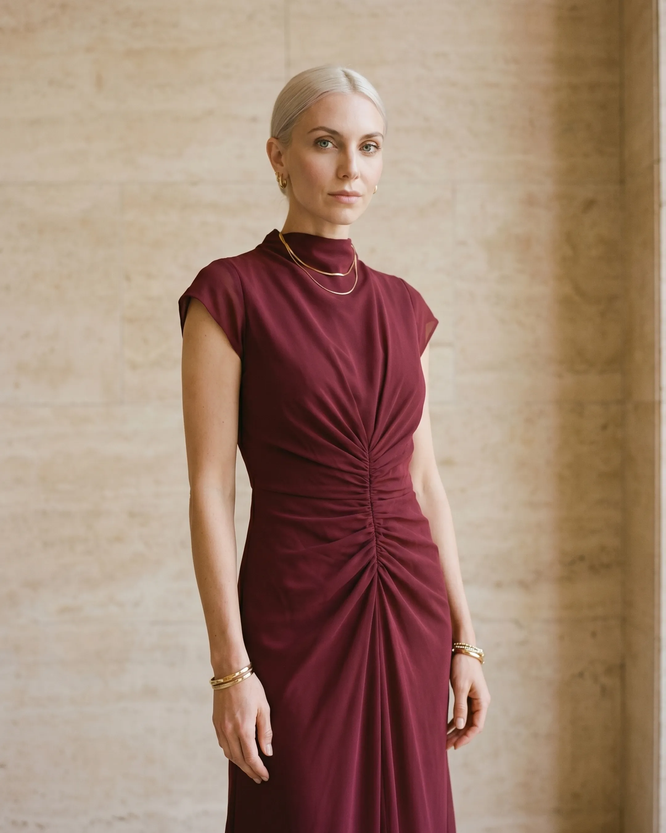 Bodice detail of the Hugo Caesar Tassi Claudia gown in Porpora wine-red chiffon, showing the draped mock neckline, cap sleeves and centre-front ruching in a Roman travertine studio