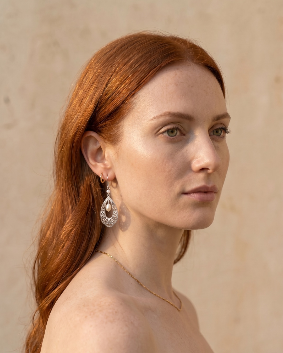Hugo Caesar Tassi Fortuna silver filigree teardrop earring with a natural pearl worn at the ear against a warm travertine wall