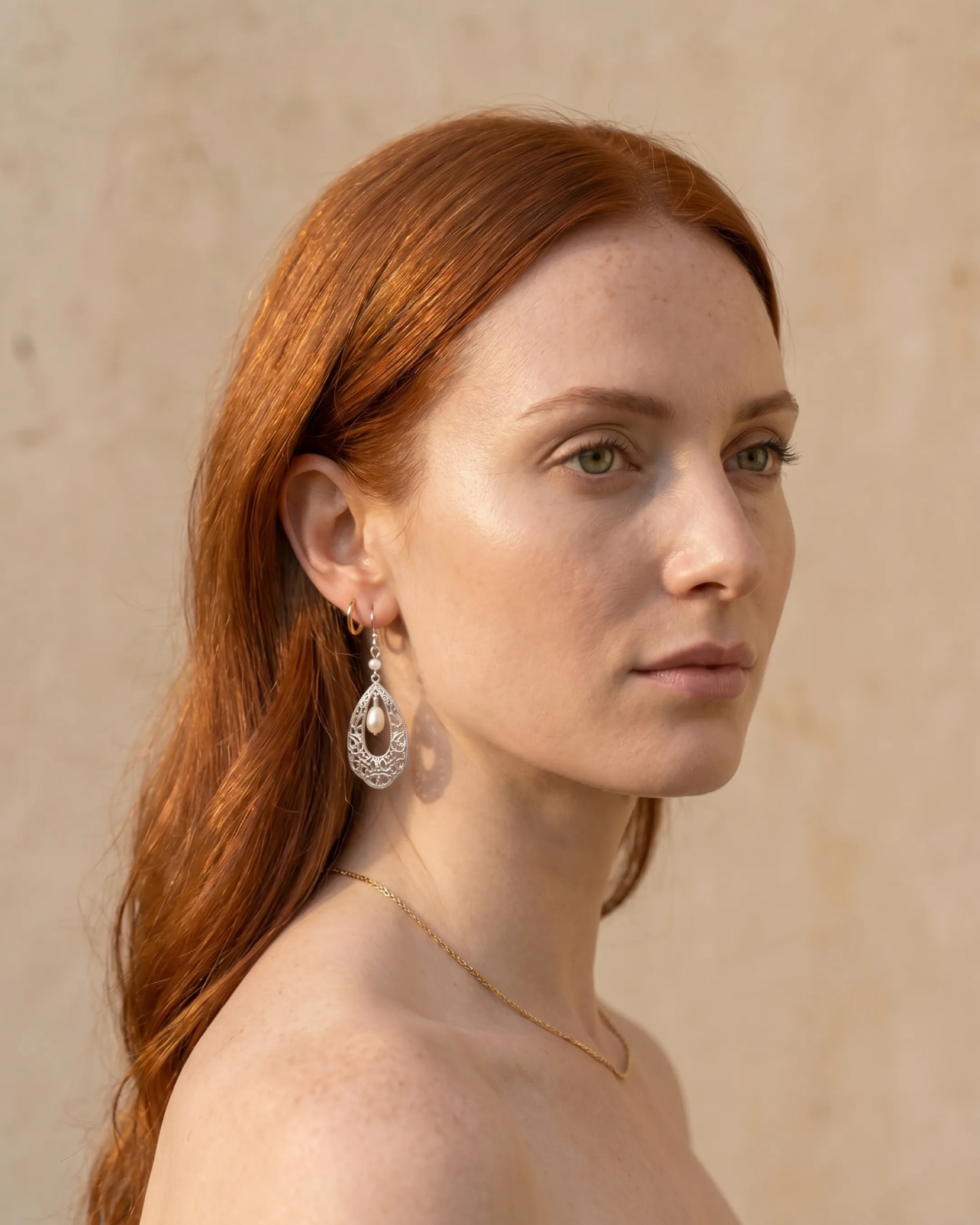 Hugo Caesar Tassi Fortuna silver filigree teardrop earring with a natural pearl worn at the ear against a warm travertine wall