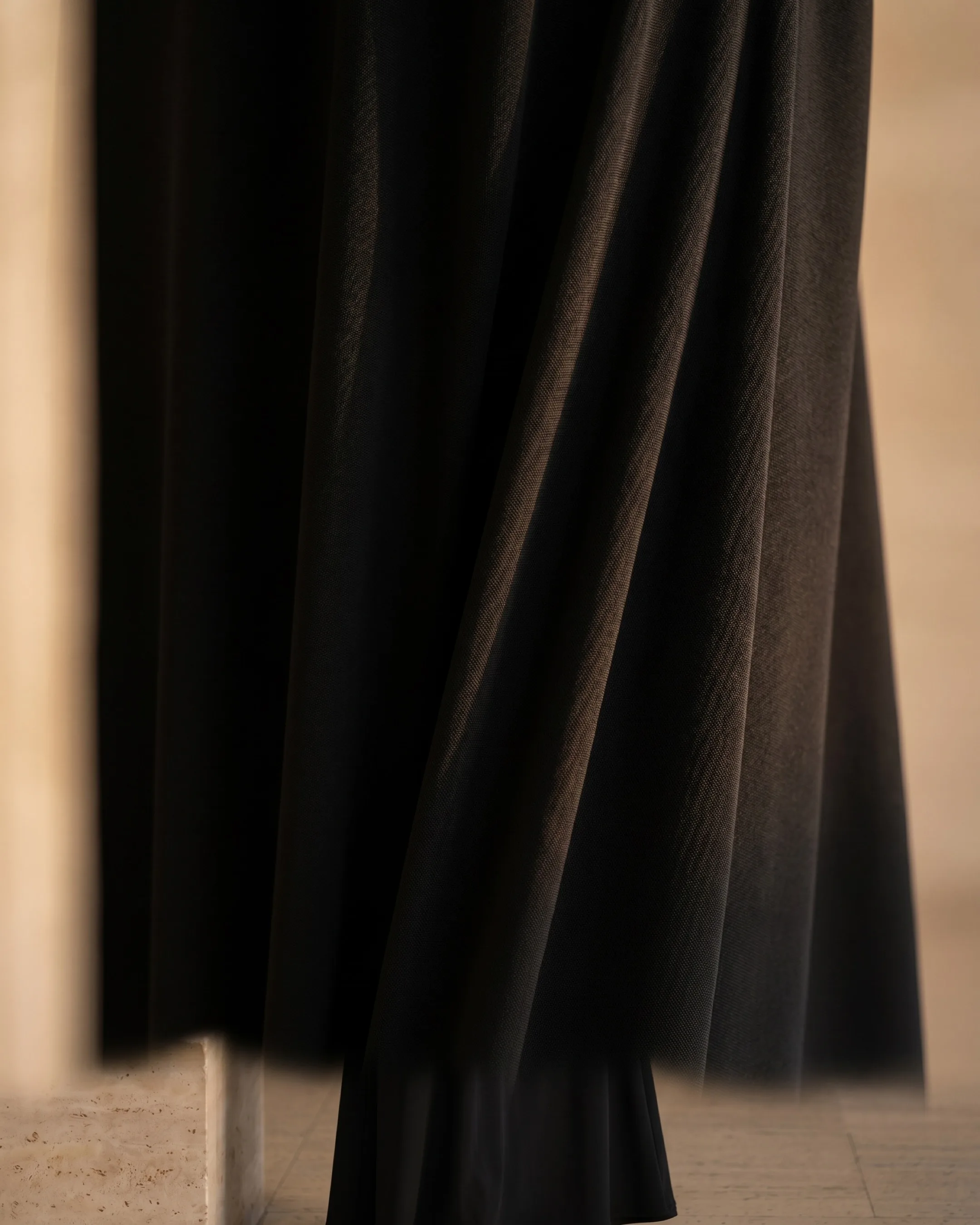 Hugo Caesar Tassi Galla macro of soft matte black crepe jersey in fluid folds, catching gentle golden light