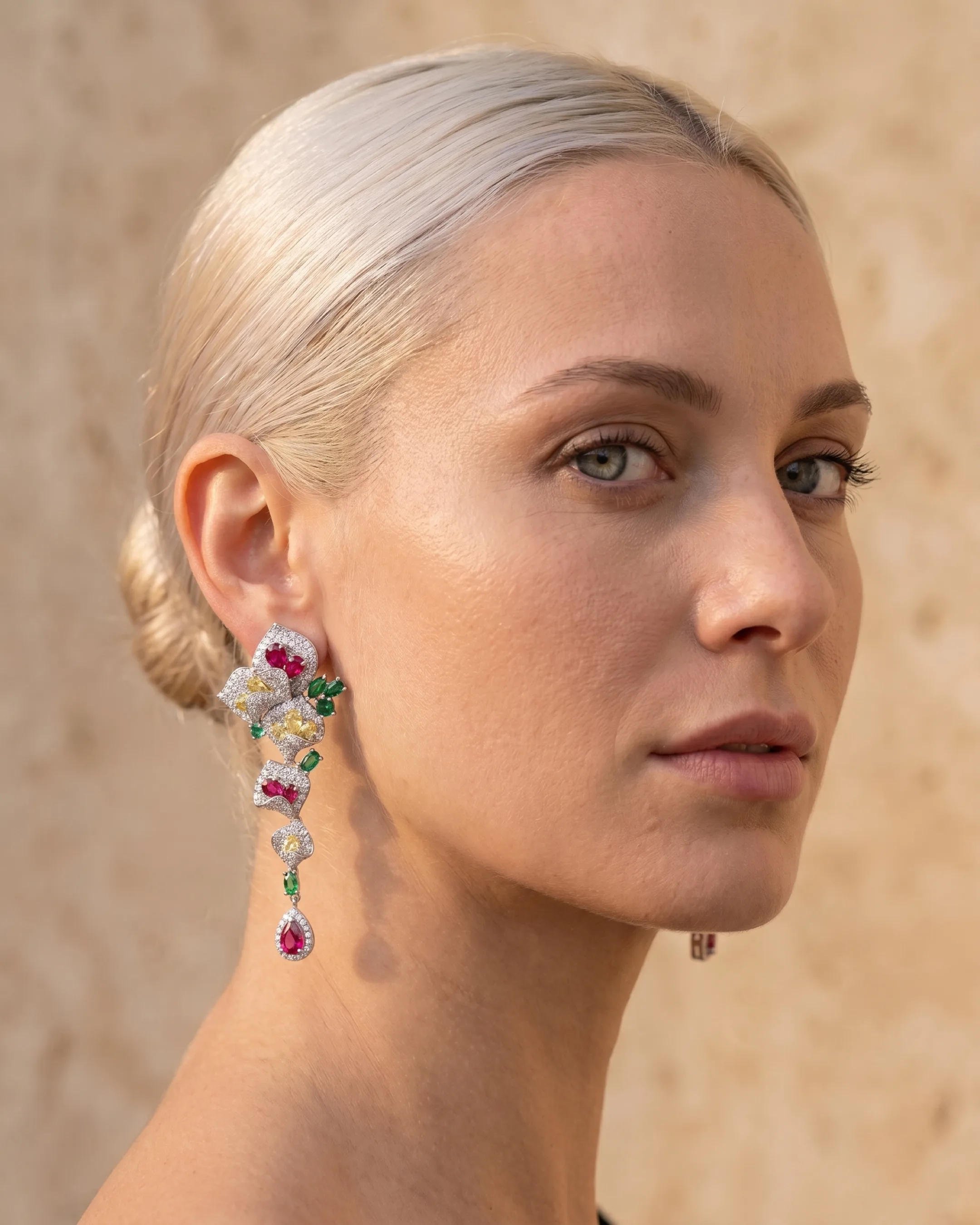 Hugo Caesar Tassi Gemma silver crystal cascade drop earring worn long against the neck beside a warm travertine wall