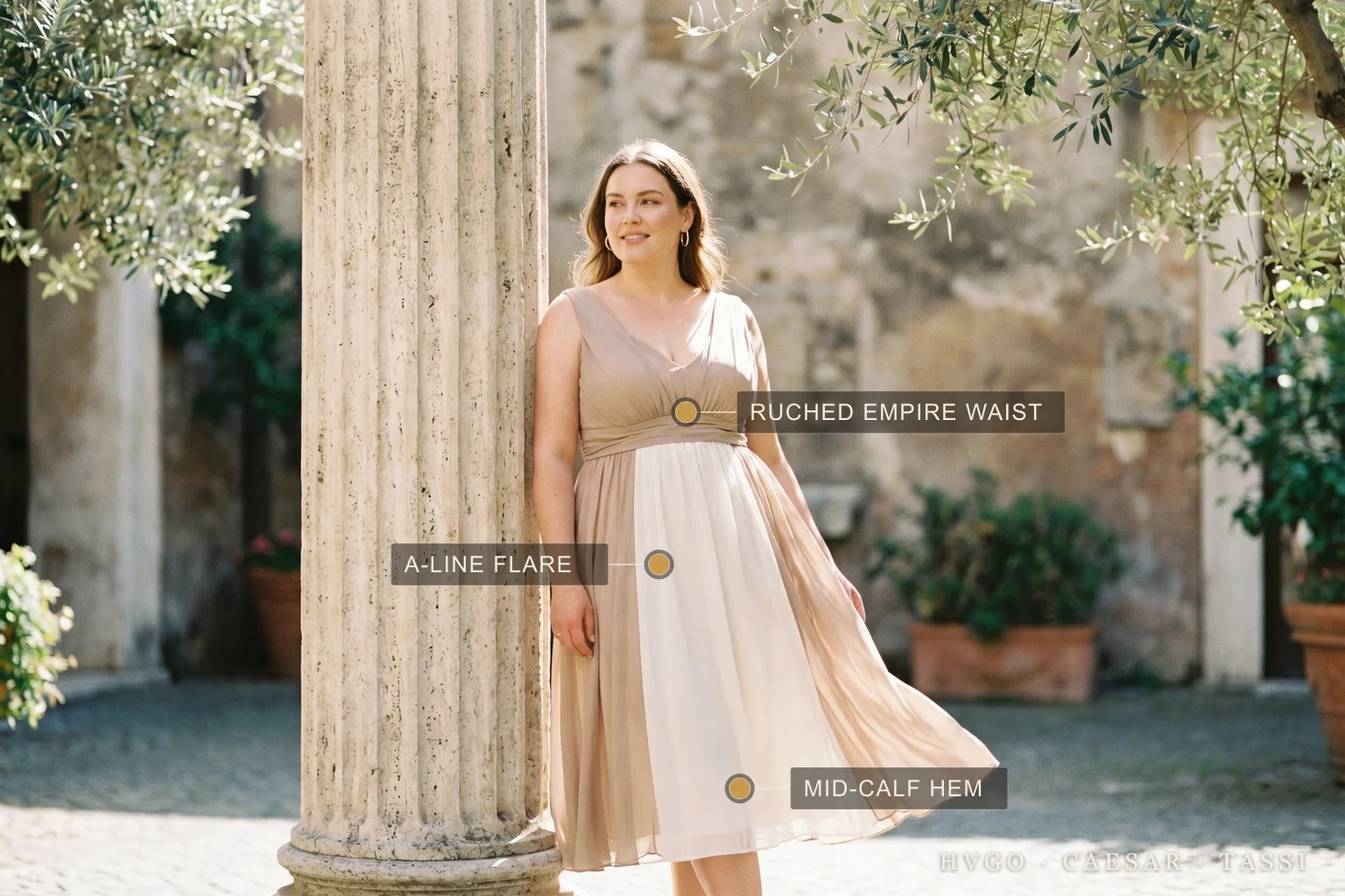 A woman with an apple body shape in a Hugo Caesar Tassi A-line chiffon midi dress in soft Travertine, labelled to show the ruched empire waist, the A-line flaring past the hip and the mid-calf hem, in a sunlit Roman courtyard