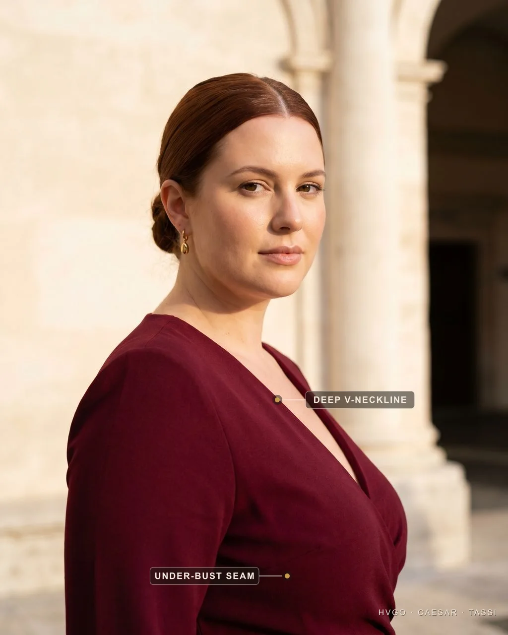Close view of a woman with an apple body shape in a deep V-neck Porpora crepe gown, labelled to show the deep V-neckline opening the chest and the seam sitting under the bust