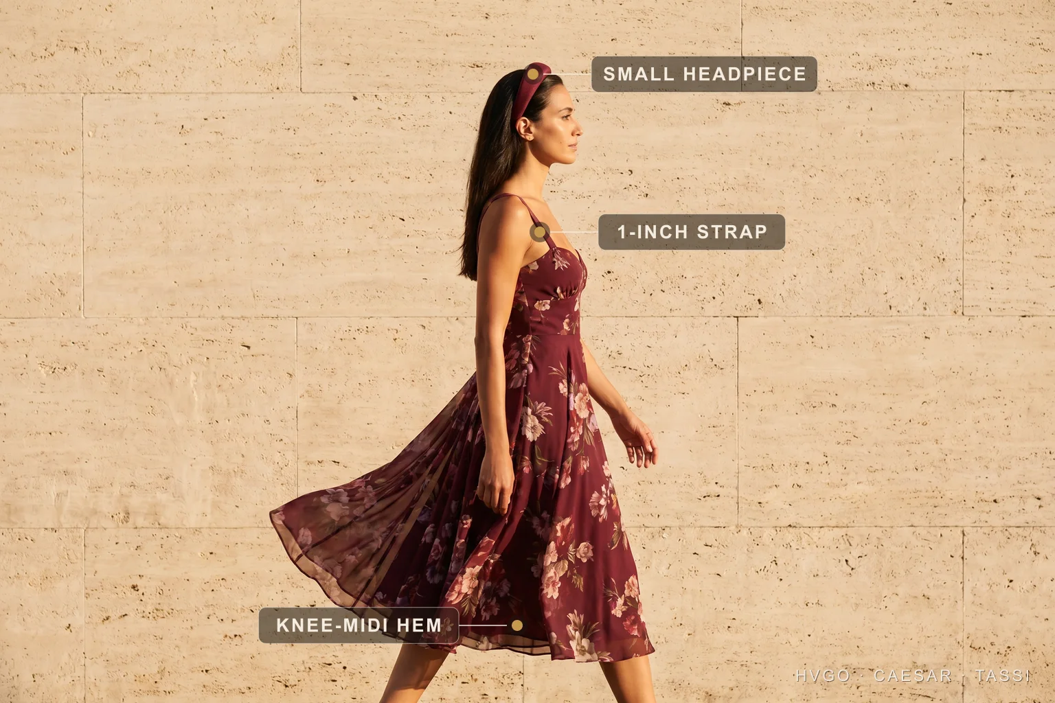 Royal Ascot small headpiece with a floral chiffon midi — Hugo Caesar Tassi Chiara in a Hugo Caesar Tassi Porpora wine floral-print chiffon midi dress with a small matching headpiece, walking mid-stride so the chiffon skirt lifts, labelled to show the small headpiece, the one-inch strap and the knee-to-midi hem, in a sunlit Roman travertine setting
