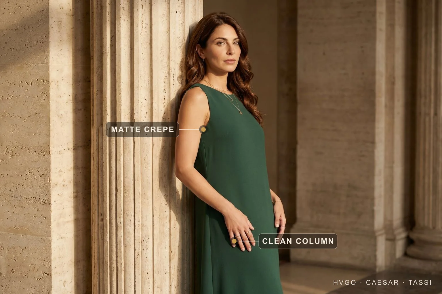 Matte crepe column gown — chiffon, satin and crepe decoded | Hugo Caesar Tassi Model in a forest-green matte crepe column gown leaning against a Roman travertine column, with baked labels marking the Matte crepe surface on the bodice and the Clean column line of the skirt.
