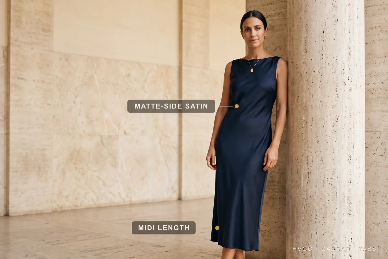 What cocktail attire means for women — Hugo Caesar Tassi Marisol in a Hugo Caesar Tassi deep-navy matte-side satin midi cocktail sheath, standing in a relaxed three-quarter contrapposto beside a fluted travertine column, labelled to show the matte-side satin fabric and the mid-calf midi length, in a warm Roman travertine colonnade