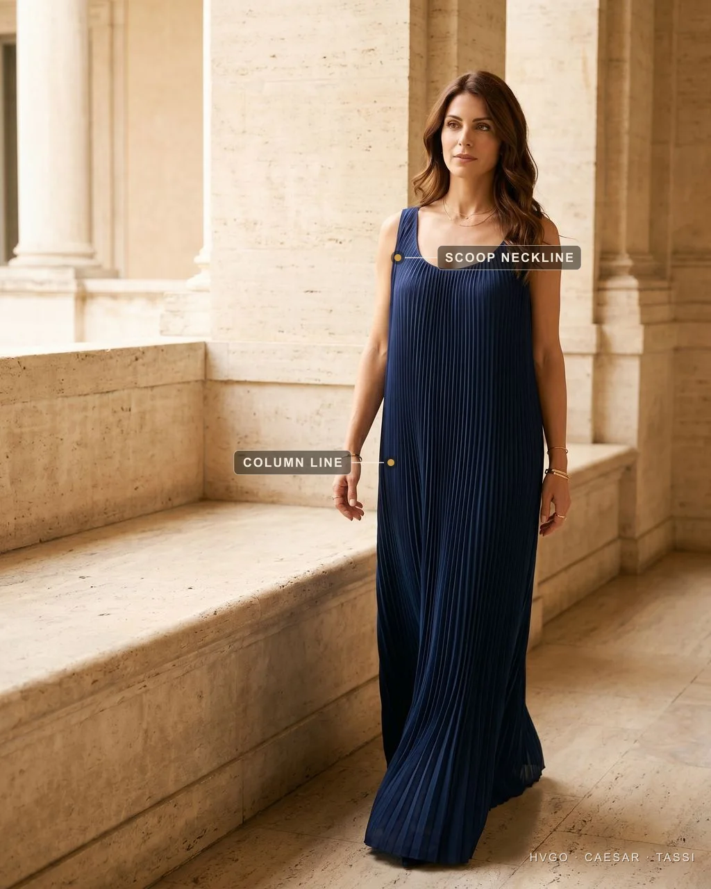 Italian model walking in a Cobalto navy Tullia knife-pleated column evening gown in a travertine loggia; labels mark the Scoop neckline and the unbroken Column line of the pleats.