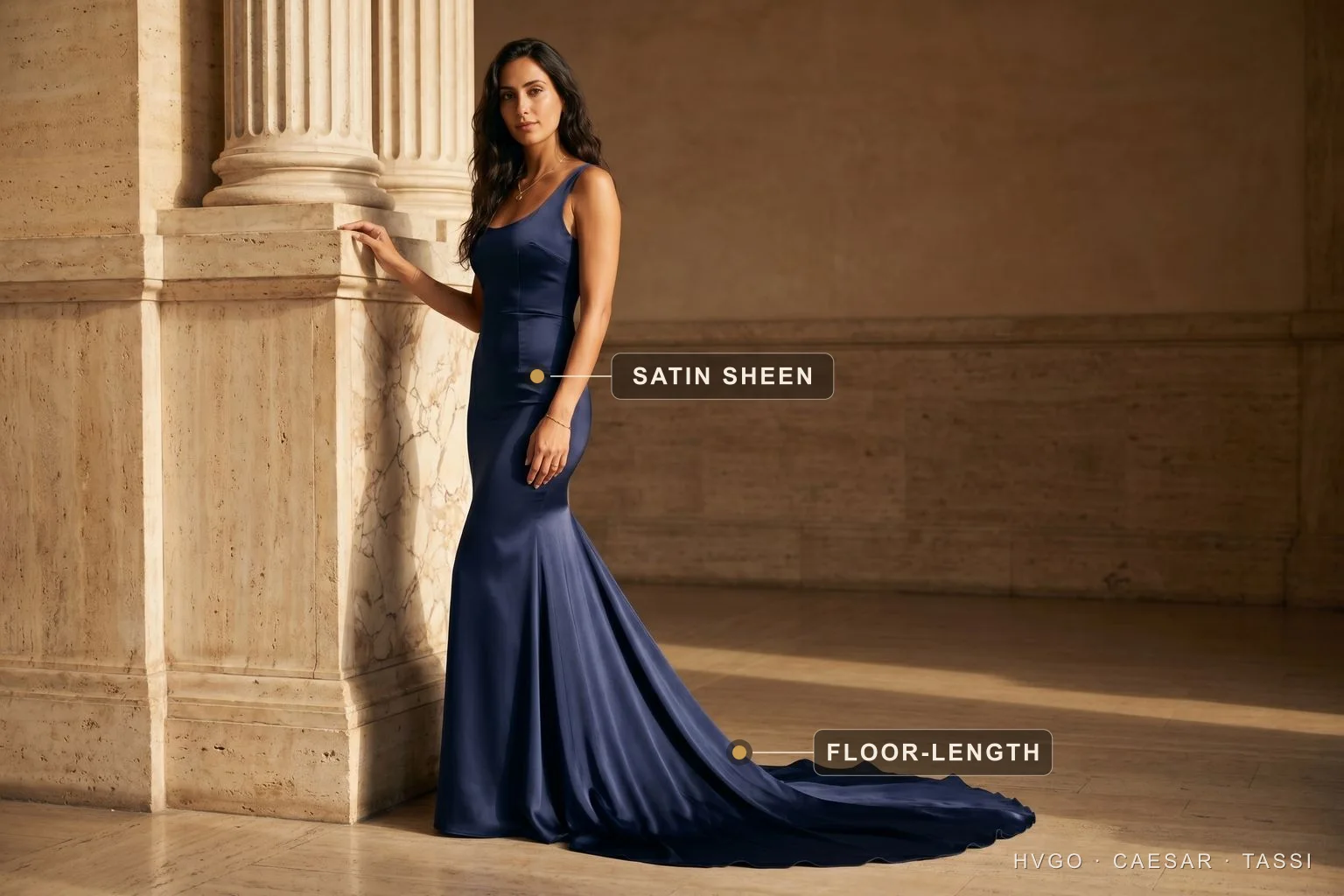What to Wear to Any Event: the formality ladder | Hugo Caesar Tassi Model Chiara in the Calpurnia fishtail satin evening gown in Cobalto navy, floor-length with a sweeping train, beside a travertine column; gilt labels mark the satin sheen on the bodice and the floor-length train — the top rung of the occasion formality ladder.