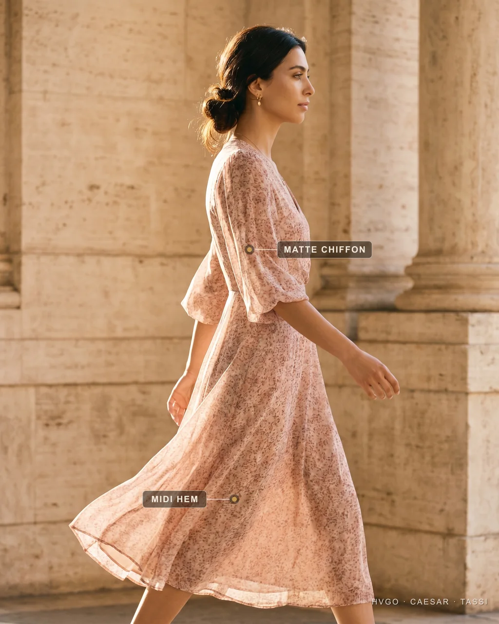 Daytime occasion dressing: chiffon midi | Hugo Caesar Tassi Model Nadia walking mid-stride in the Livilla floral-print chiffon midi in soft Cipria rose, sleeves catching the air beside a travertine column; gilt labels mark the matte chiffon fabric and the midi hem — the daytime/cocktail rung of the ladder.