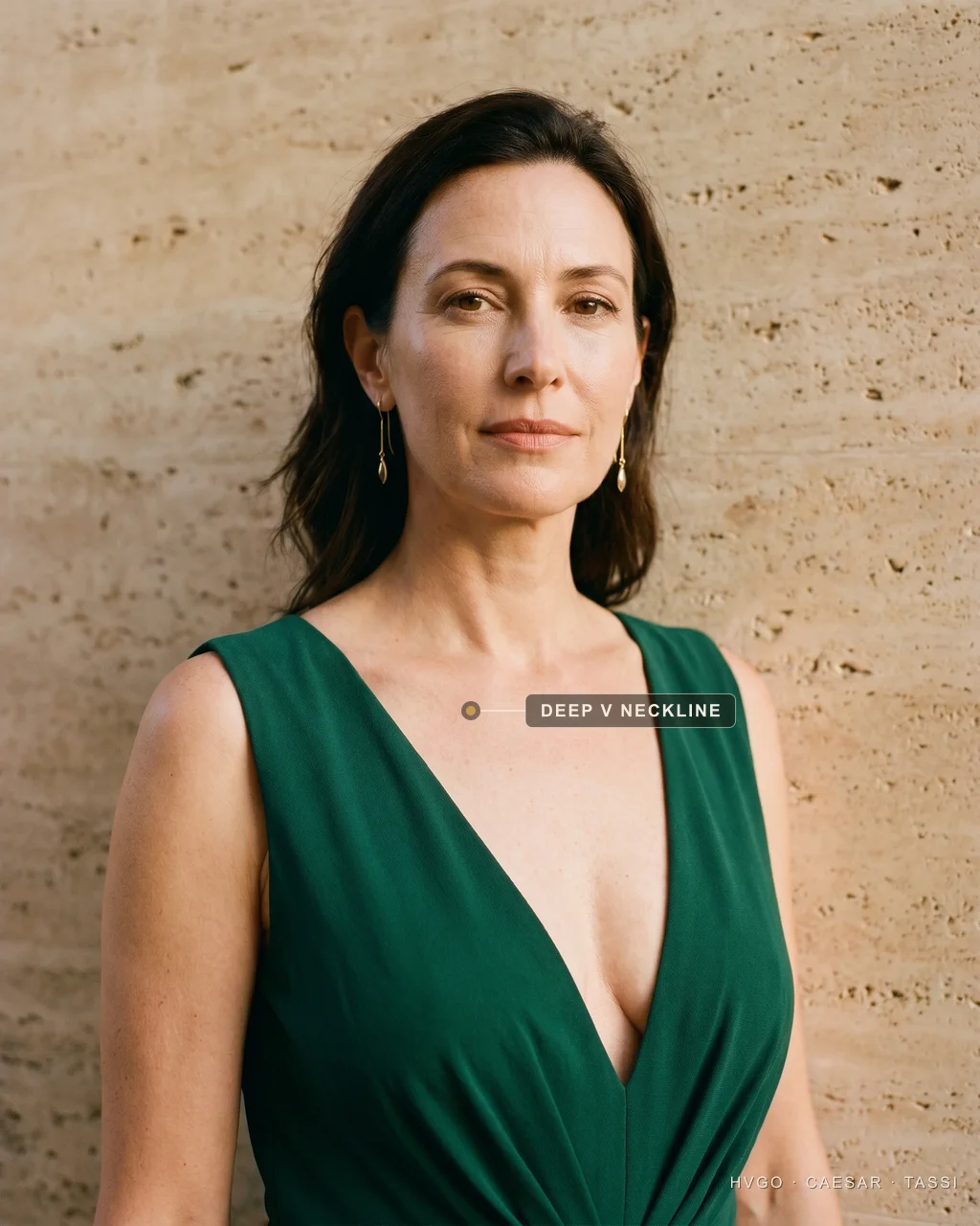 Deep V-neckline for an inverted-triangle figure — Hugo Caesar Tassi Close view of a woman with an inverted-triangle figure in a Hugo Caesar Tassi emerald gown with a deep V-neckline, labelled to show the V drawing a vertical and narrowing the shoulder line