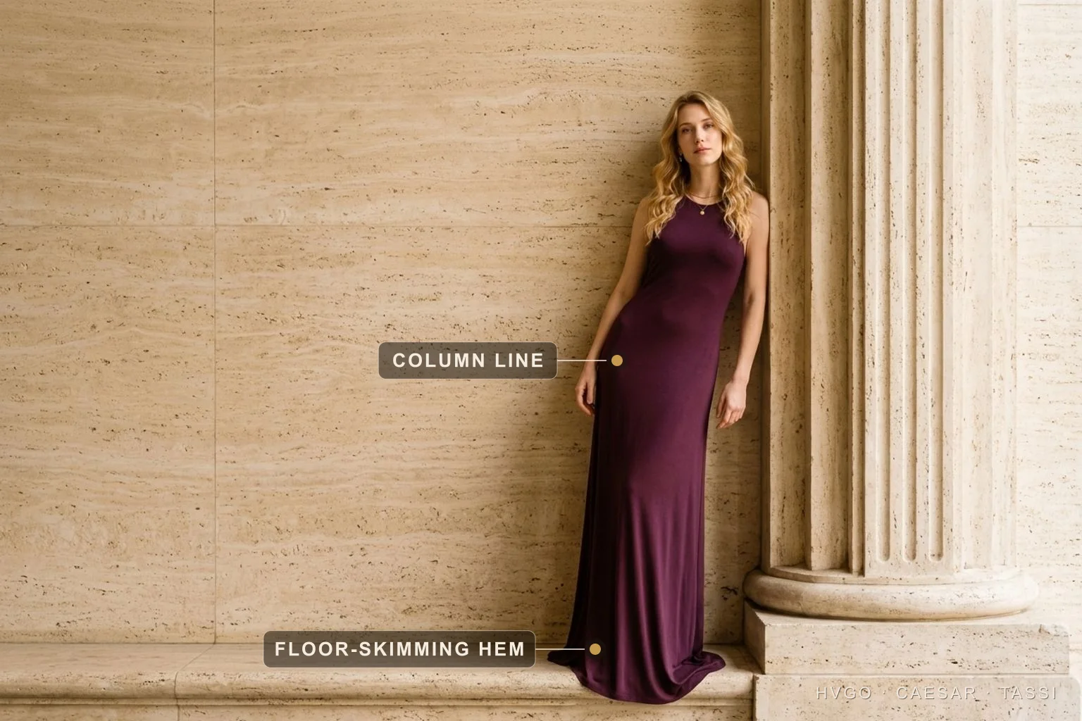 Maxi Dress Length: The Floor-Skimming Column Hem — Hugo Caesar Tassi Bianca leaning off-centre against a travertine ledge beside a fluted Roman column in a deep aubergine wine draped column maxi, the baked markers marking the floor-skimming hem pooling at her feet and the unbroken column line of the gown.