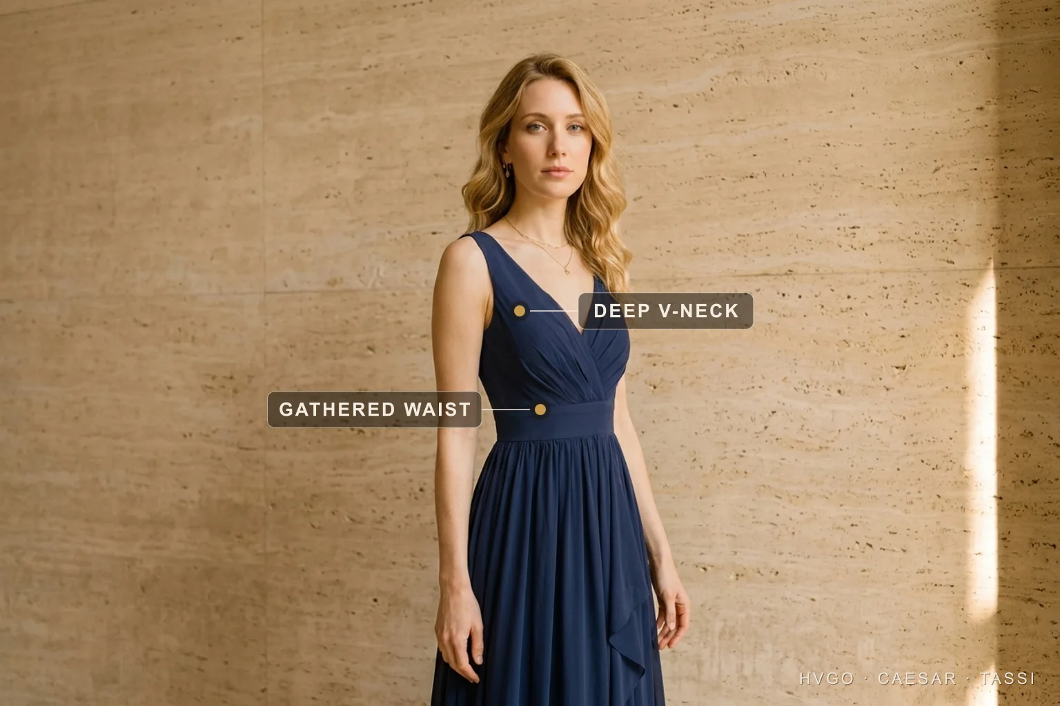Dress necklines explained — the deep V-neck — Hugo Caesar Tassi A woman in a Hugo Caesar Tassi navy deep V-neck pleated chiffon evening gown, labelled to show the deep V-neckline opening a downward line at the chest and the gathered waist seam, in a Roman travertine studio