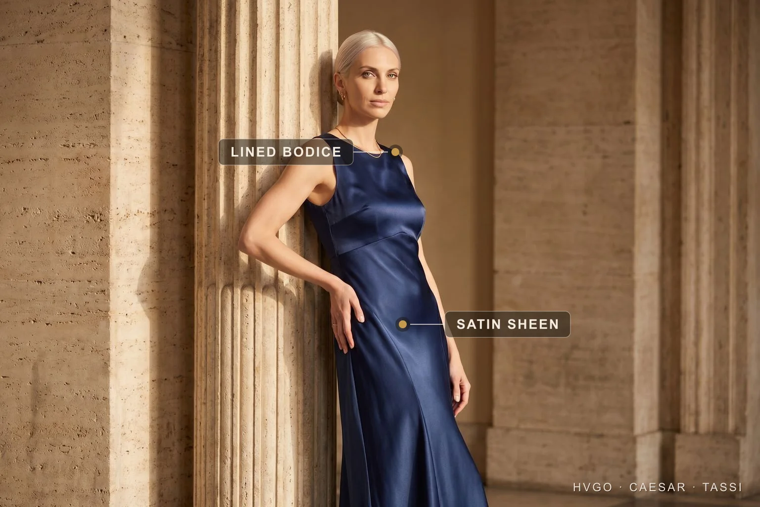 How to care for a satin occasion dress — Hugo Caesar Tassi A model in a navy silk-satin occasion gown leaning against a travertine column, with markers calling out the fitted lined bodice and the lustrous bias-cut satin sheen of the skirt.