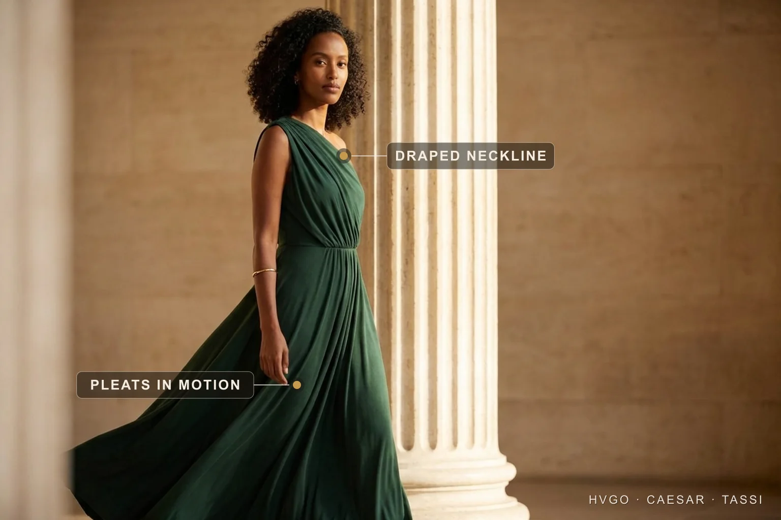 Aisha, an HCT house model with natural dark curls, caught walking mid-stride in a deep Verde-Antico forest-green one-shoulder draped Grecian column gown so the pleated skirt sweeps in motion, placed off-centre beside a tall fluted Roman travertine column, labelled to show the draped one-shoulder neckline and the pleats in motion