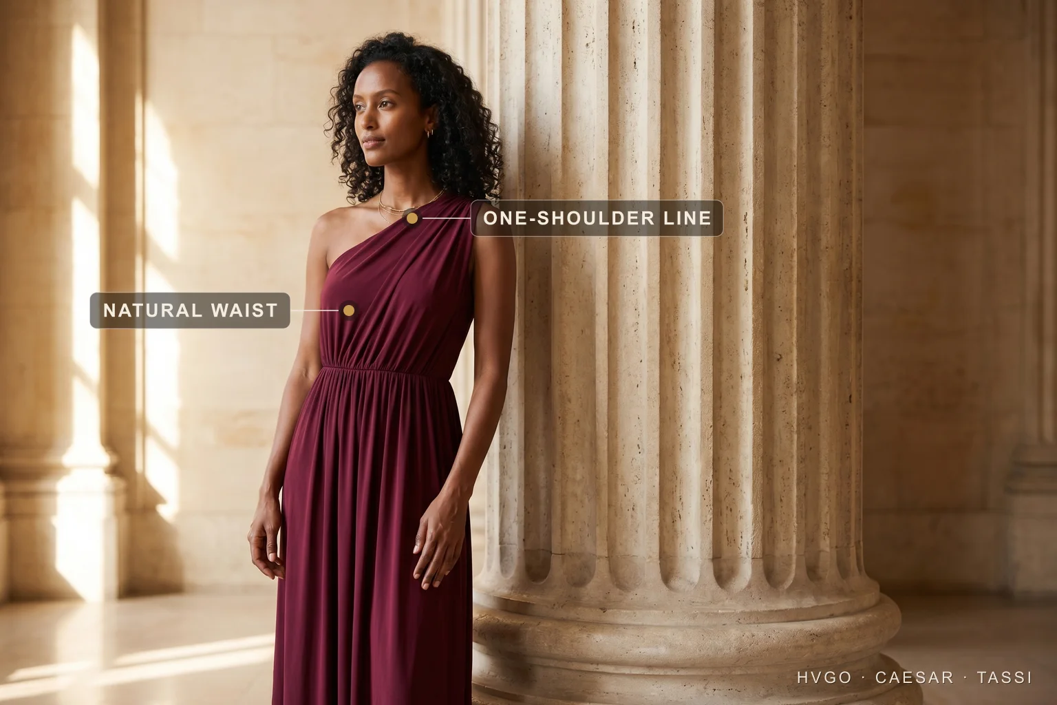 Roman influence on modern fashion: the one-shoulder column gown — Hugo Caesar Tassi Model in a deep Porpora wine one-shoulder Grecian column gown leaning beside a fluted travertine column, with markers on the one-shoulder diagonal drape line and the gathered natural waist.