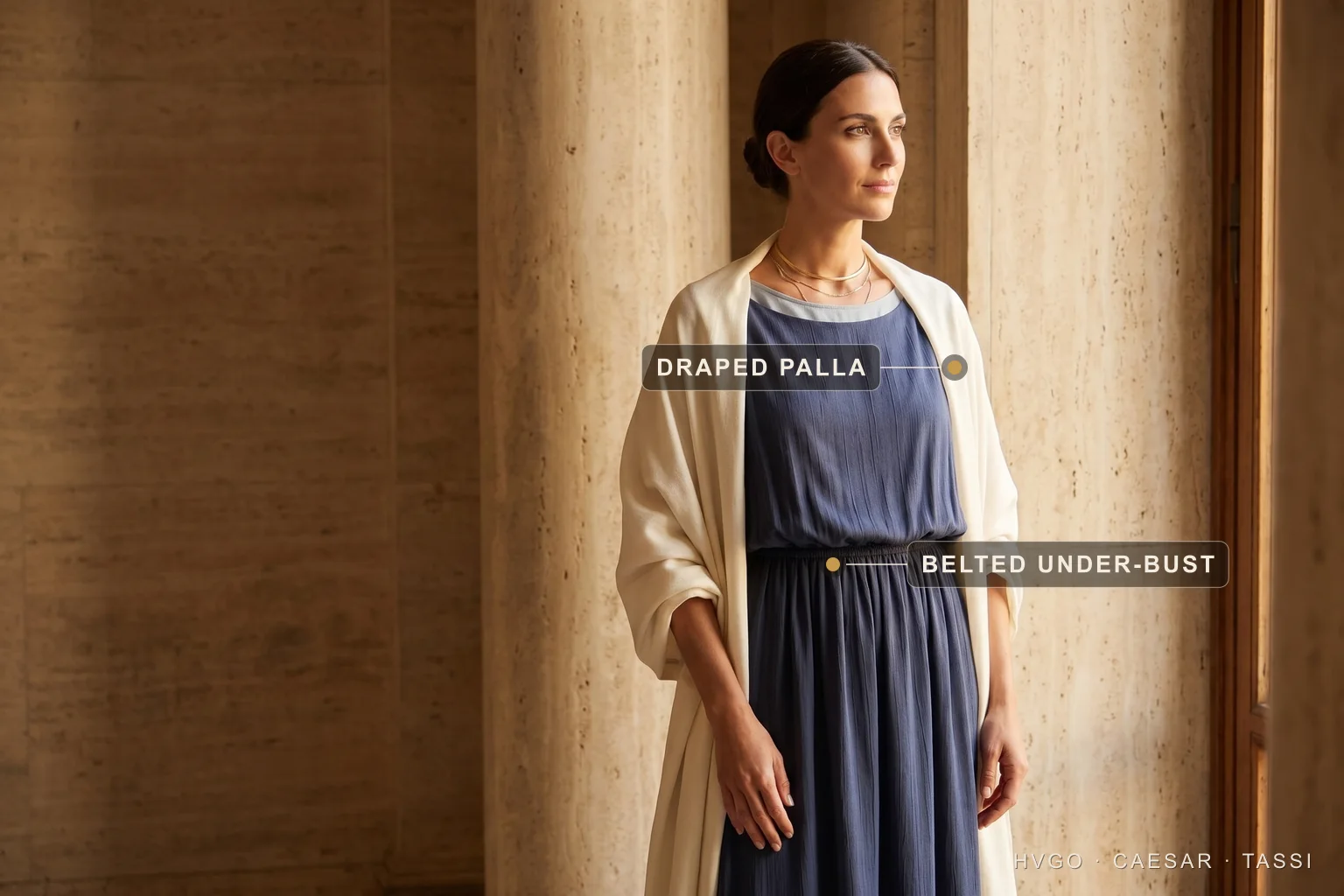 The stola, tunica and palla layered column — Hugo Caesar Tassi A model in a Roman-inspired layered column: a navy stola gathered high and belted under the bust, with an ivory palla draped over the shoulders, labelled 'Draped palla' on the ivory wrap and 'Belted under-bust' on the gold waist belt.
