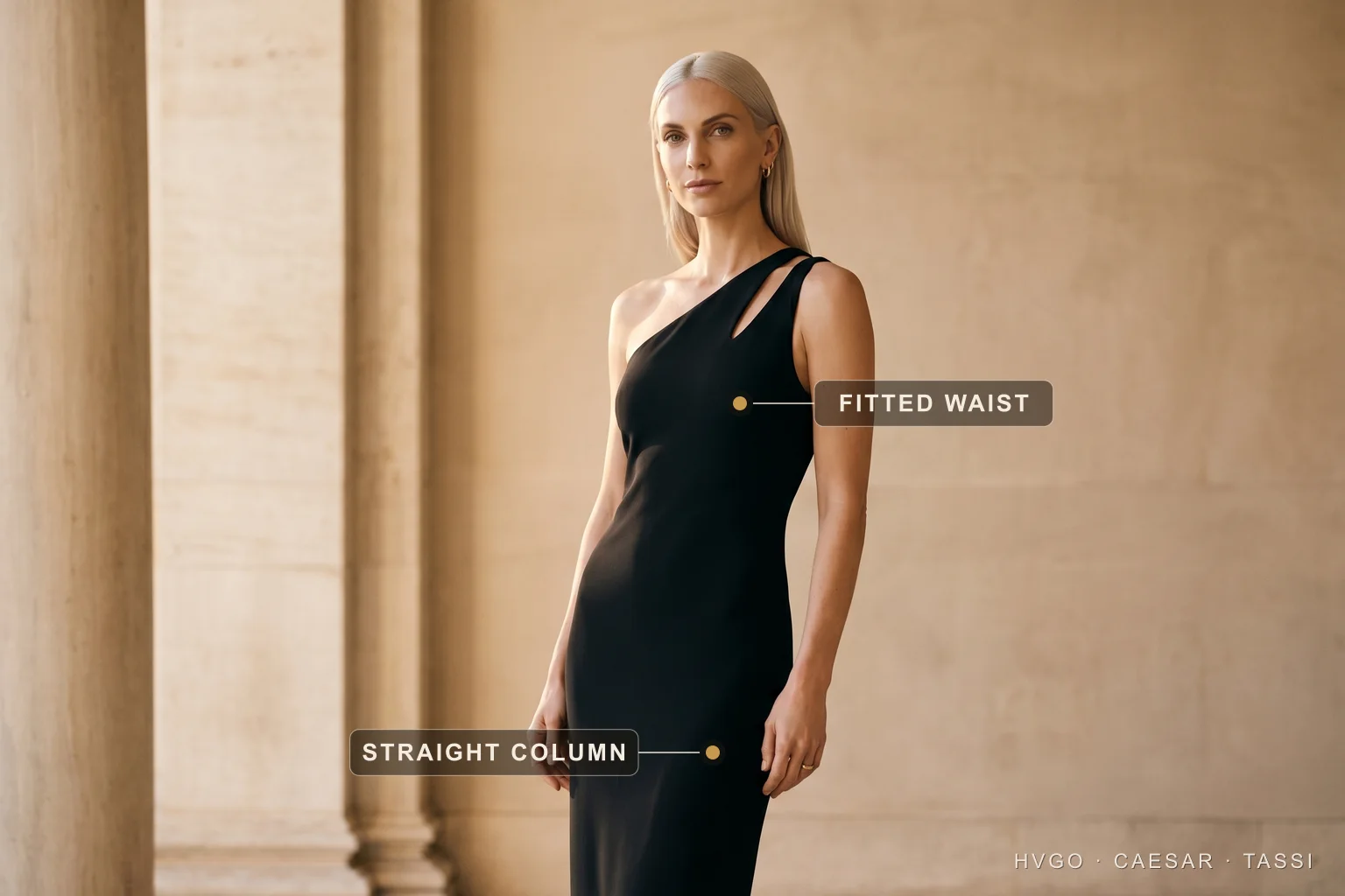 Dress silhouettes explained — the column and sheath line — Hugo Caesar Tassi A platinum-blonde woman in a Hugo Caesar Tassi Basalt-black one-shoulder matte-crepe column gown, turned three-quarters beside a Roman travertine column, labelled to show the fitted waist and the straight column skirt dropping in one unbroken vertical line