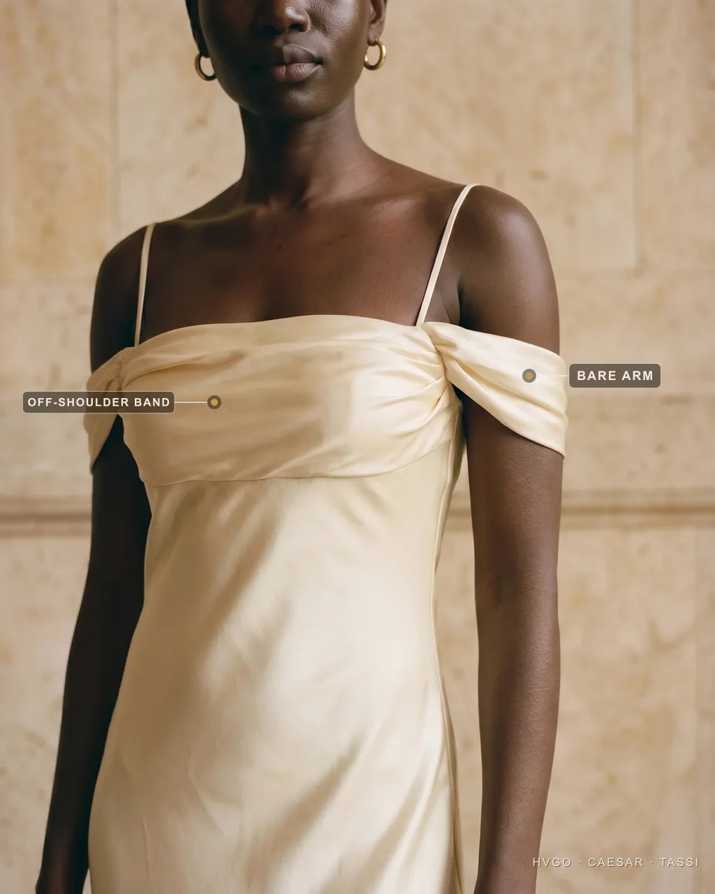 Dress sleeve types explained — the off-the-shoulder bare-arm look — Hugo Caesar Tassi Close view of a woman in a Hugo Caesar Tassi champagne bias-cut satin off-the-shoulder gown, labelled to show the off-shoulder Bardot band sitting below the shoulders and the bare upper arm