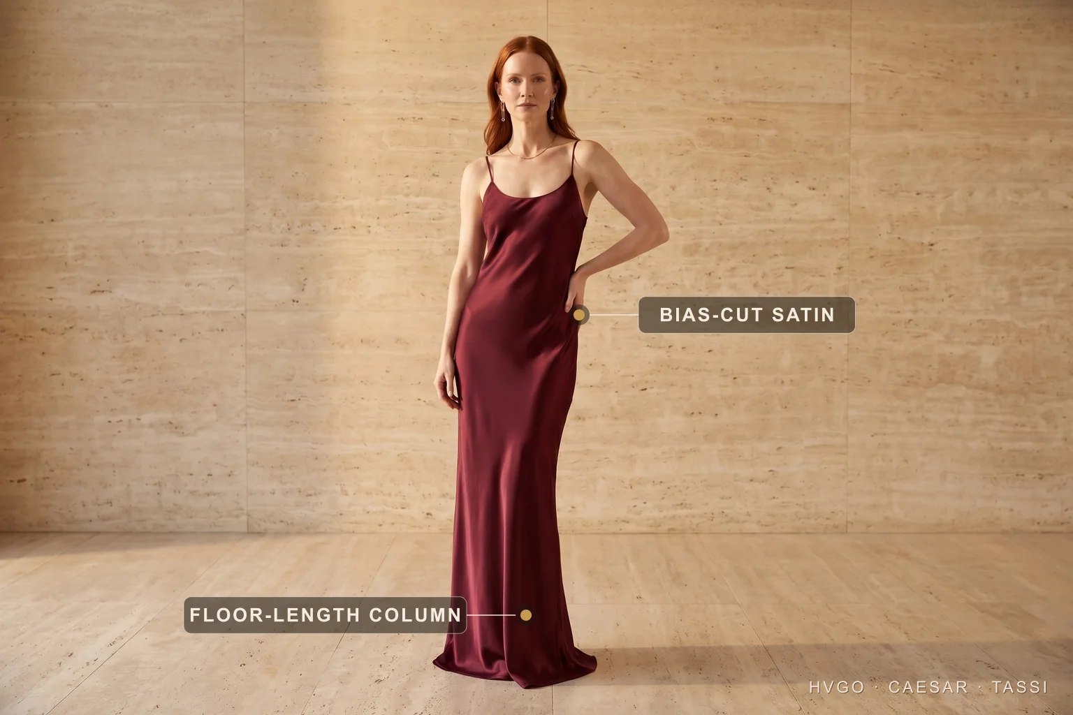 Black-tie wedding guest satin gown — Hugo Caesar Tassi A wedding guest in a Hugo Caesar Tassi deep-wine bias-cut satin column gown in a Roman travertine studio, labelled to show the bias-cut satin and the floor-length column hem — the black-tie answer