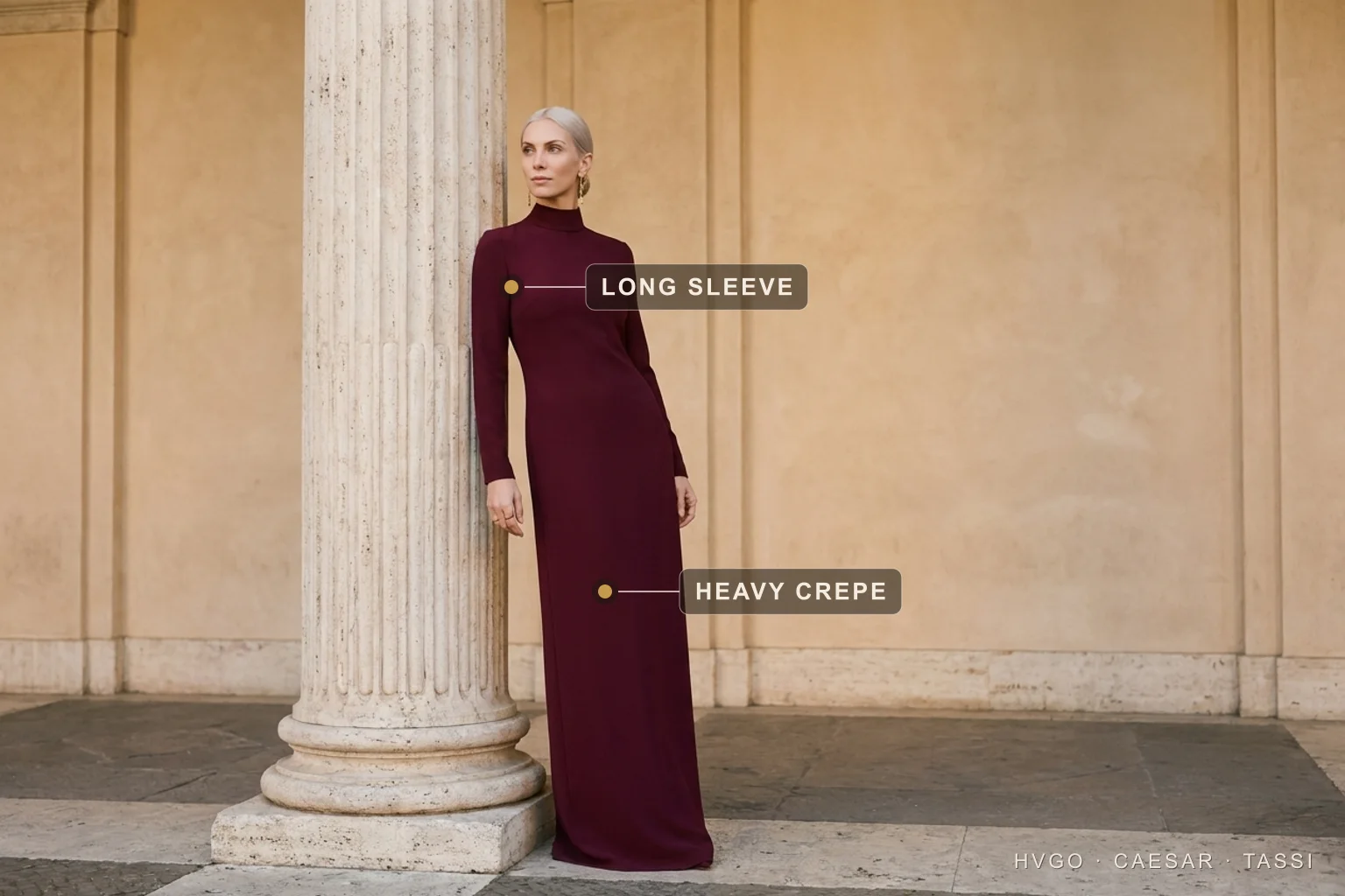 Wine Long-Sleeve Crepe Column Gown for a Winter Wedding Guest — Hugo Caesar Tassi Valentina in a wine-burgundy long-sleeve heavy-crepe column gown standing in three-quarter contrapposto beside a fluted travertine column, gilt markers labelling the long sleeve and the heavy crepe, in a warm Roman travertine setting
