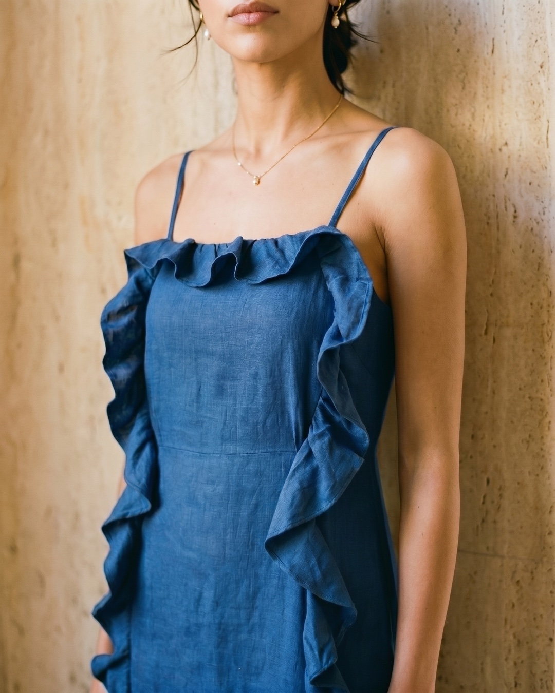 Detail of the Hugo Caesar Tassi Junia slip midi in Cobalto, showing the fine straps, ruffle-trimmed neckline and cascading side ruffle in a Roman travertine studio
