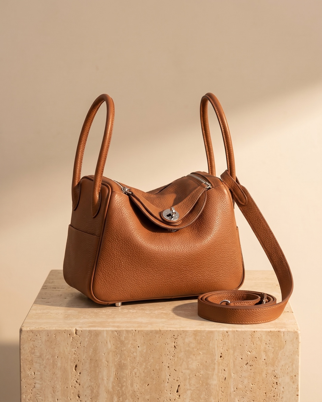 Hugo Caesar Tassi Lanuvina soft two-handle leather handbag in Cuoio cognac pebble-grain cowhide with silver turn-lock, on a warm travertine pedestal