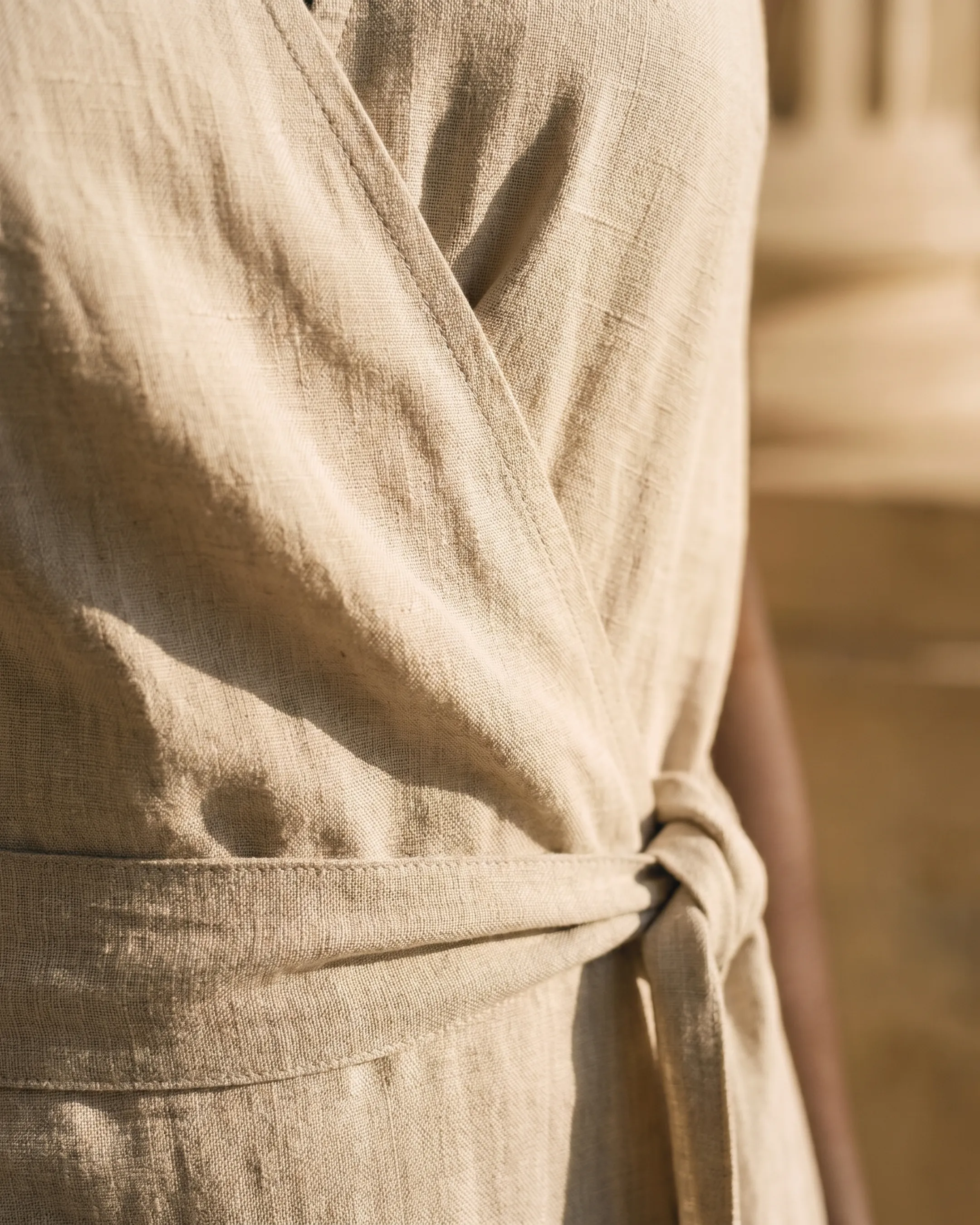 Macro detail of the Hugo Caesar Tassi Lavinia dress's matte, slubby Avorio Tencel-linen weave, the wrap overlap seam and self-fabric tie knot