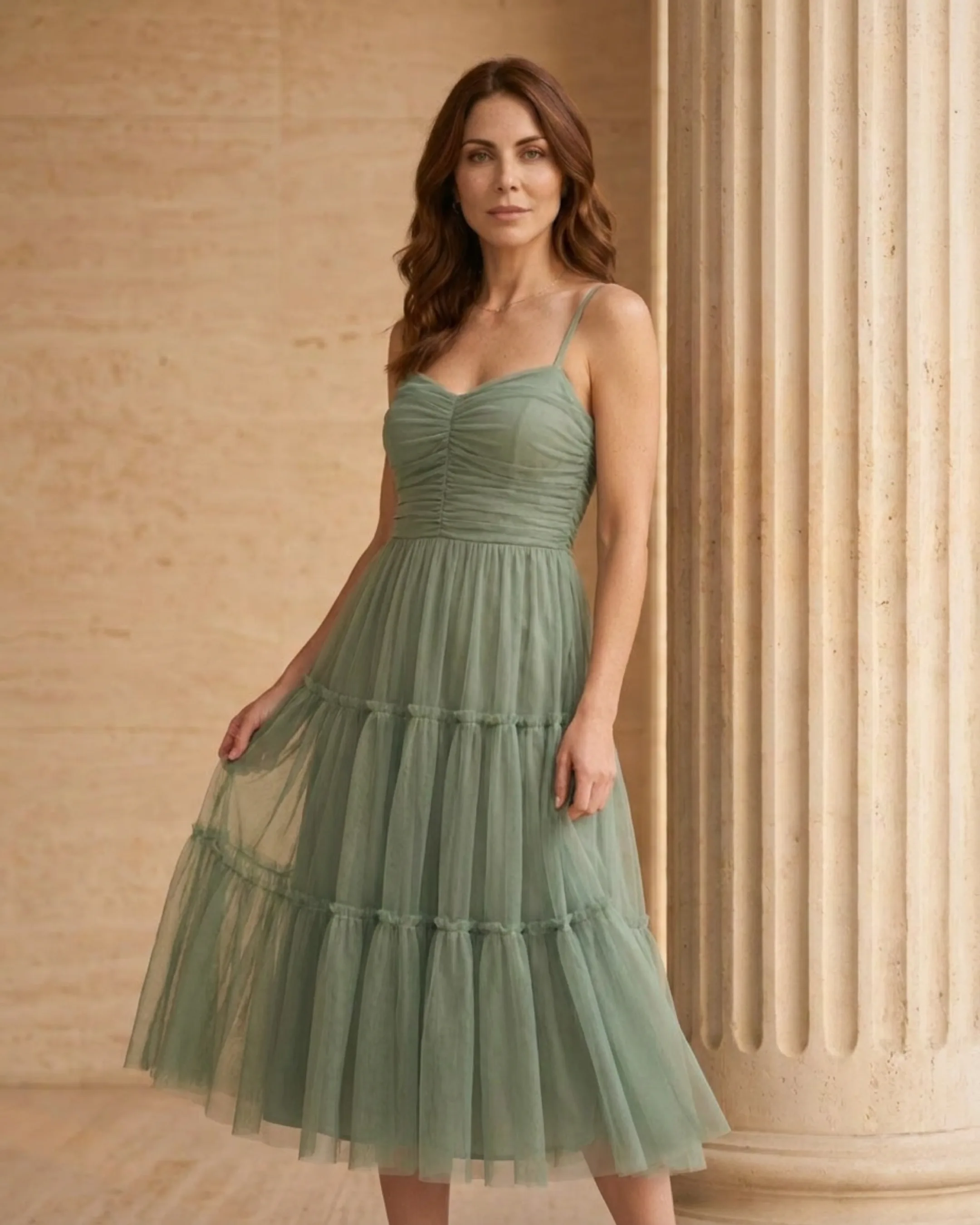 Editorial portrait of the Hugo Caesar Tassi Marcia tiered tulle tea-length dress in sage green Verde Antico among Roman travertine columns in golden light