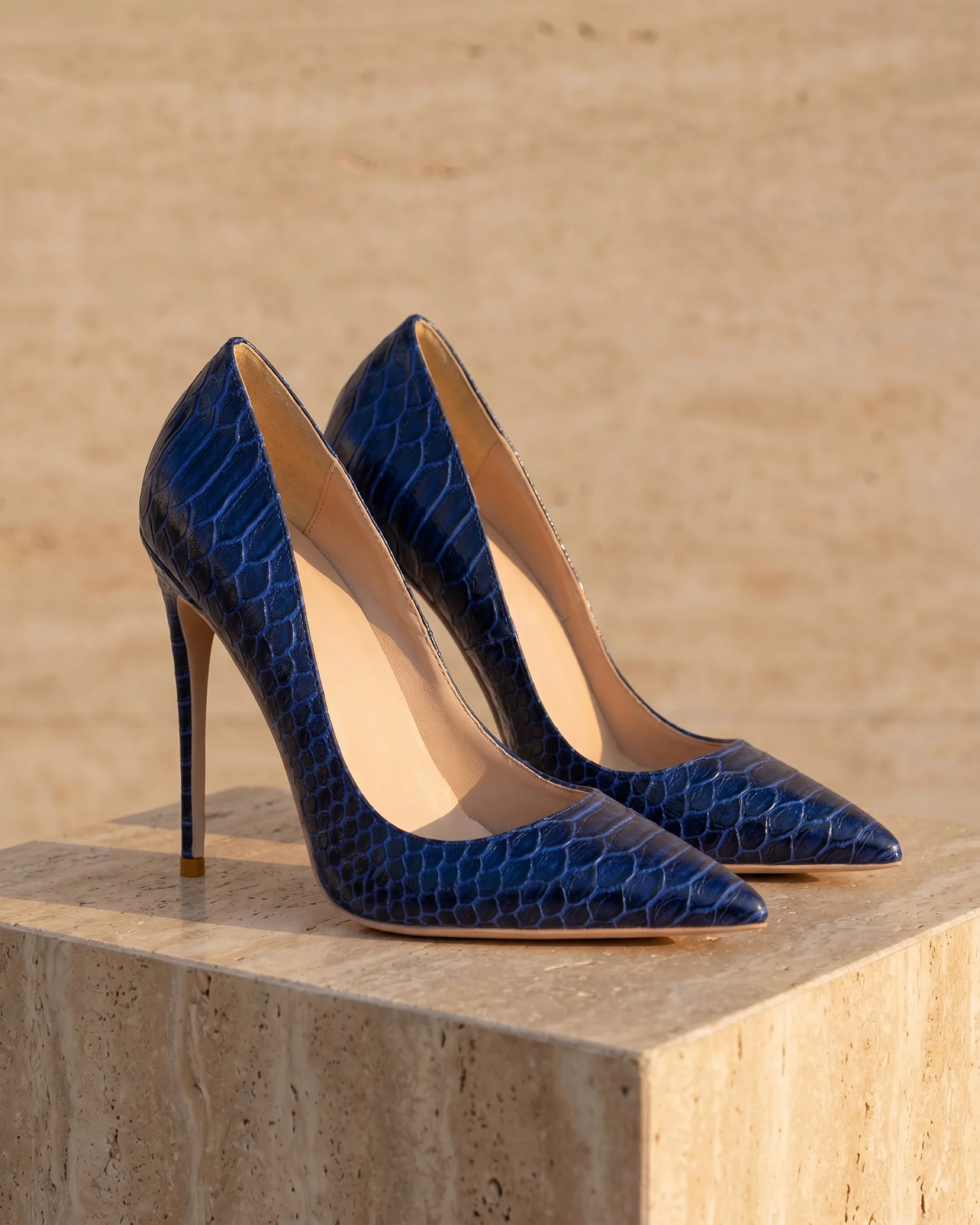 Hugo Caesar Tassi Matidia pointed-toe stiletto court pumps in Cobalto snake-embossed leather, the pair on a warm travertine pedestal