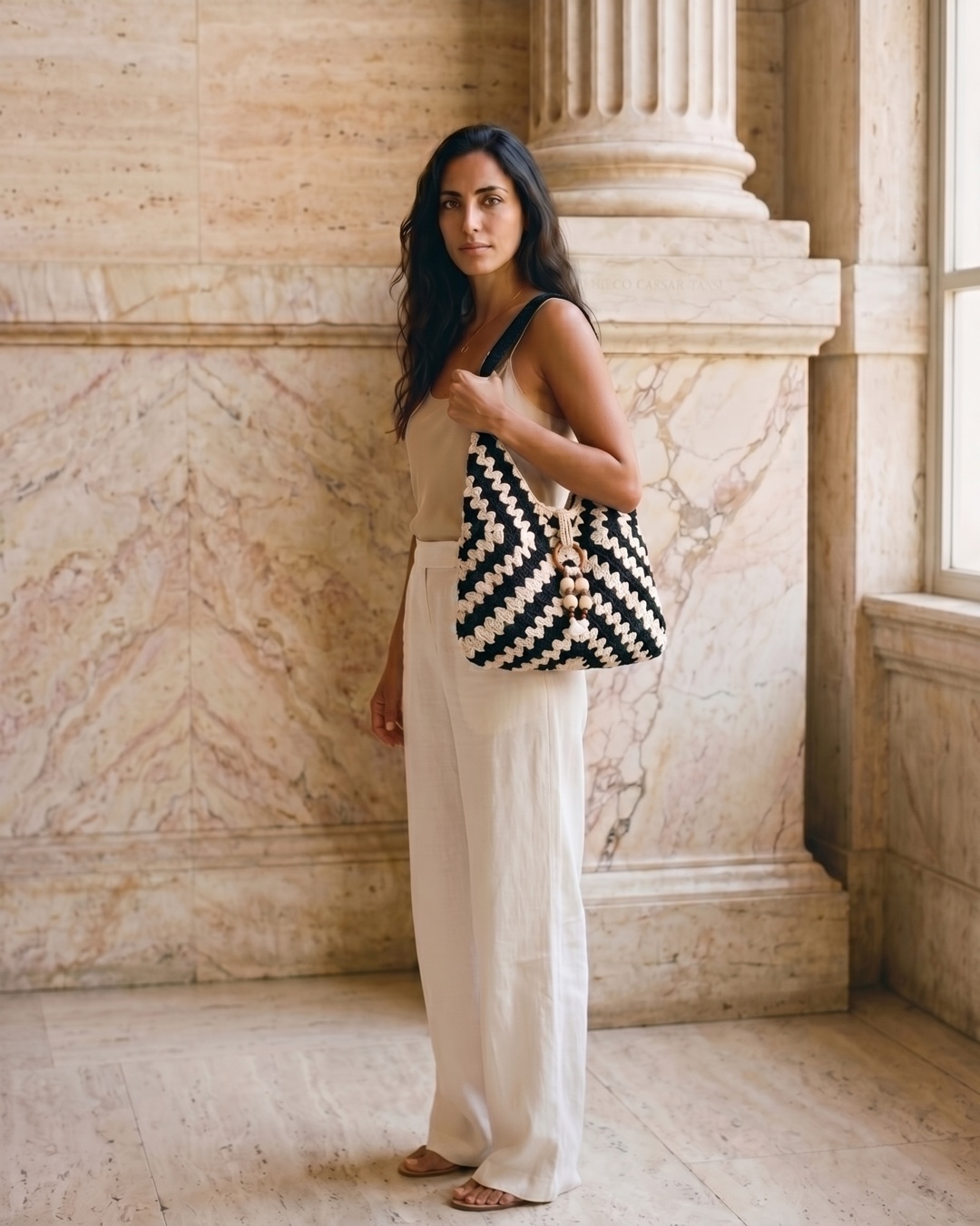 Hugo Caesar Tassi Ostia hand-crocheted woven shoulder tote in Basalt, carried by a model in a Roman travertine studio