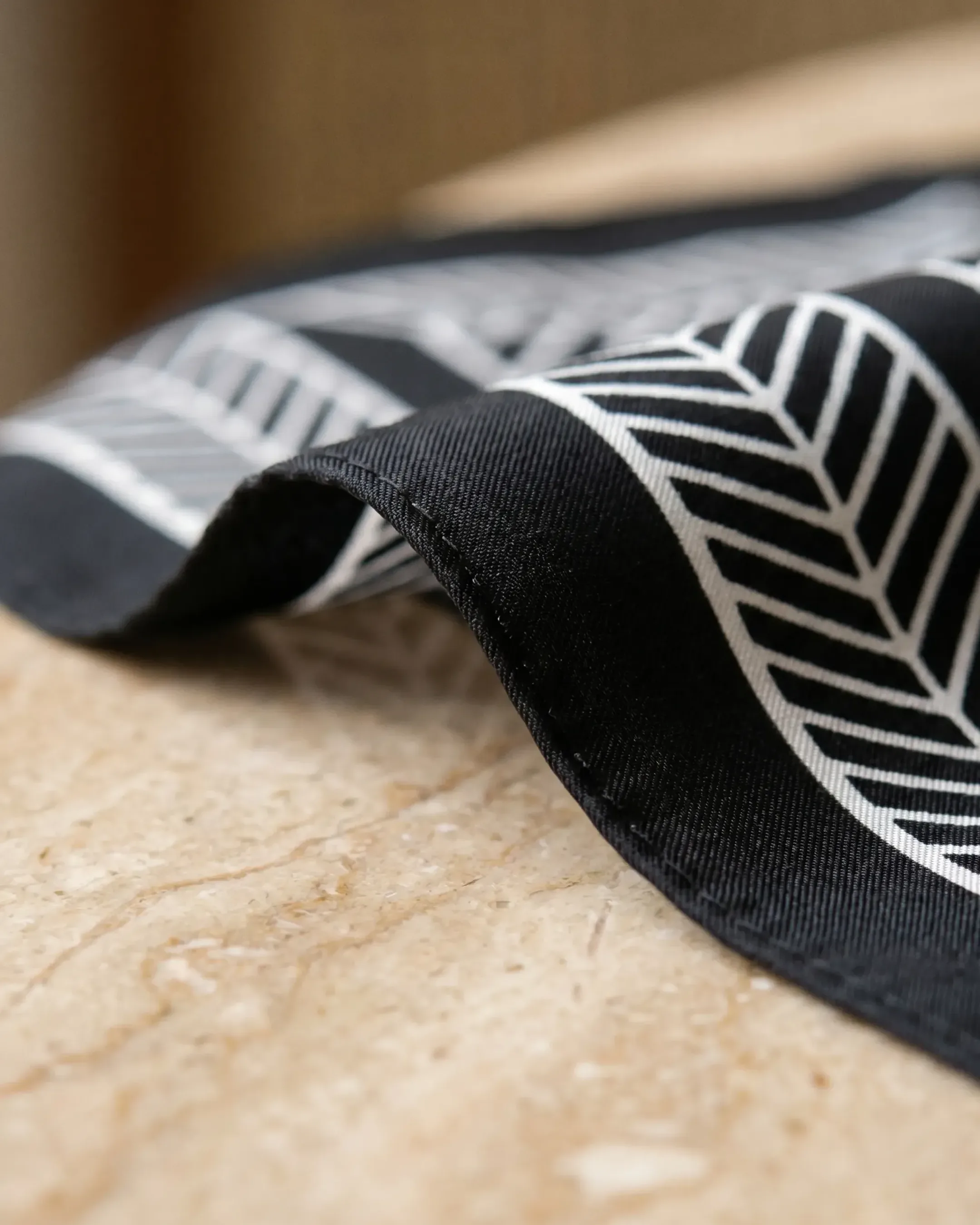 Macro detail of the Hugo Caesar Tassi Palmyra scarf hand-rolled edge and twill silk-look weave in Basalt black and Avorio ivory