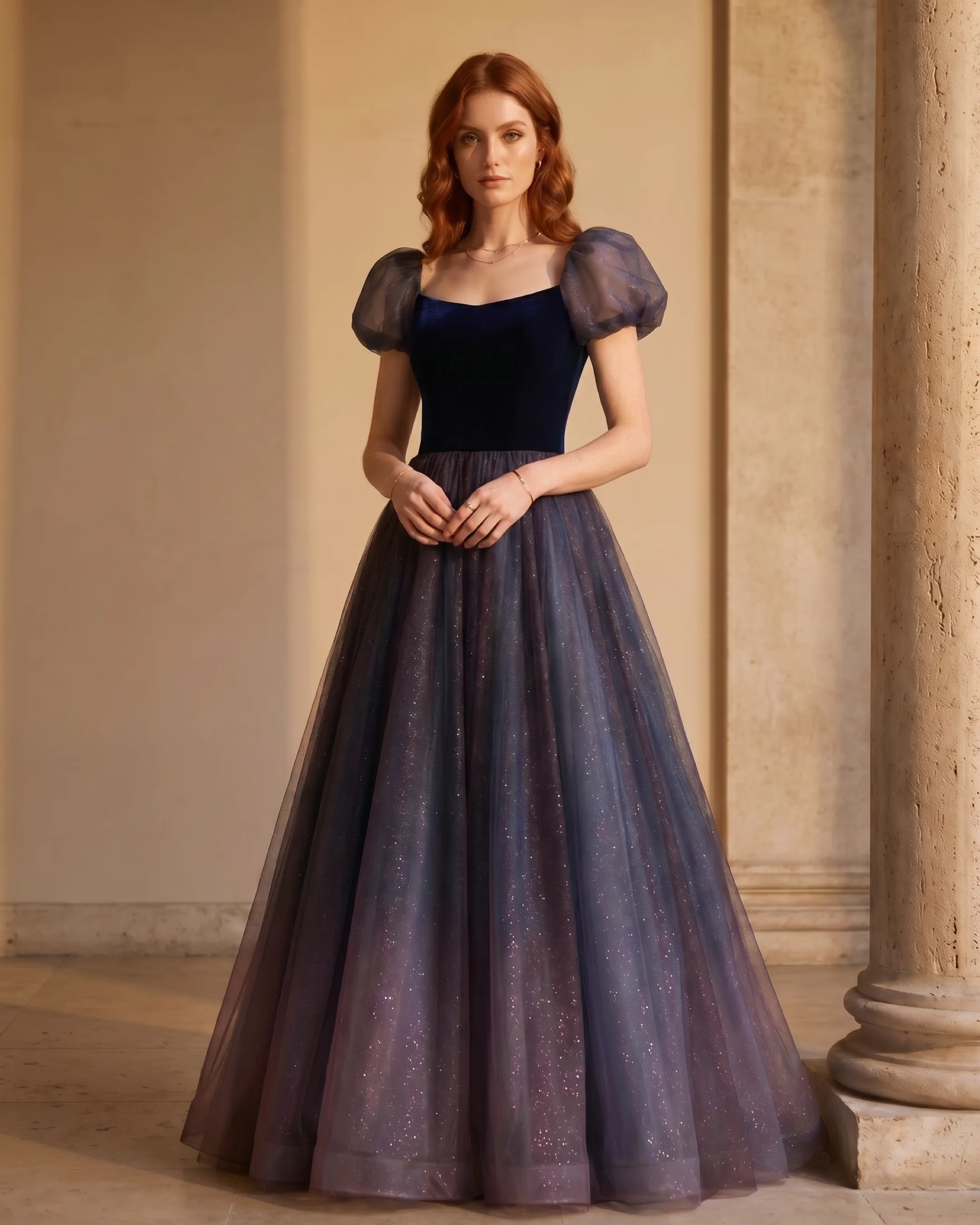 Hugo Caesar Tassi Petronia bubble-sleeve velvet-bodice ballgown in Cobalto navy galaxy tulle, full-length front view by a travertine column