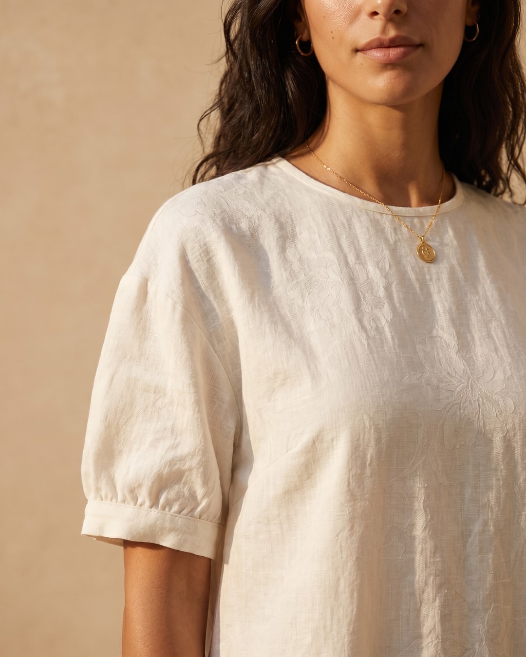 Detail of the Hugo Caesar Tassi Pomponia linen dress in Avorio, showing the round neckline, short gathered puff sleeve and tonal woven floral linen in a Roman travertine studio