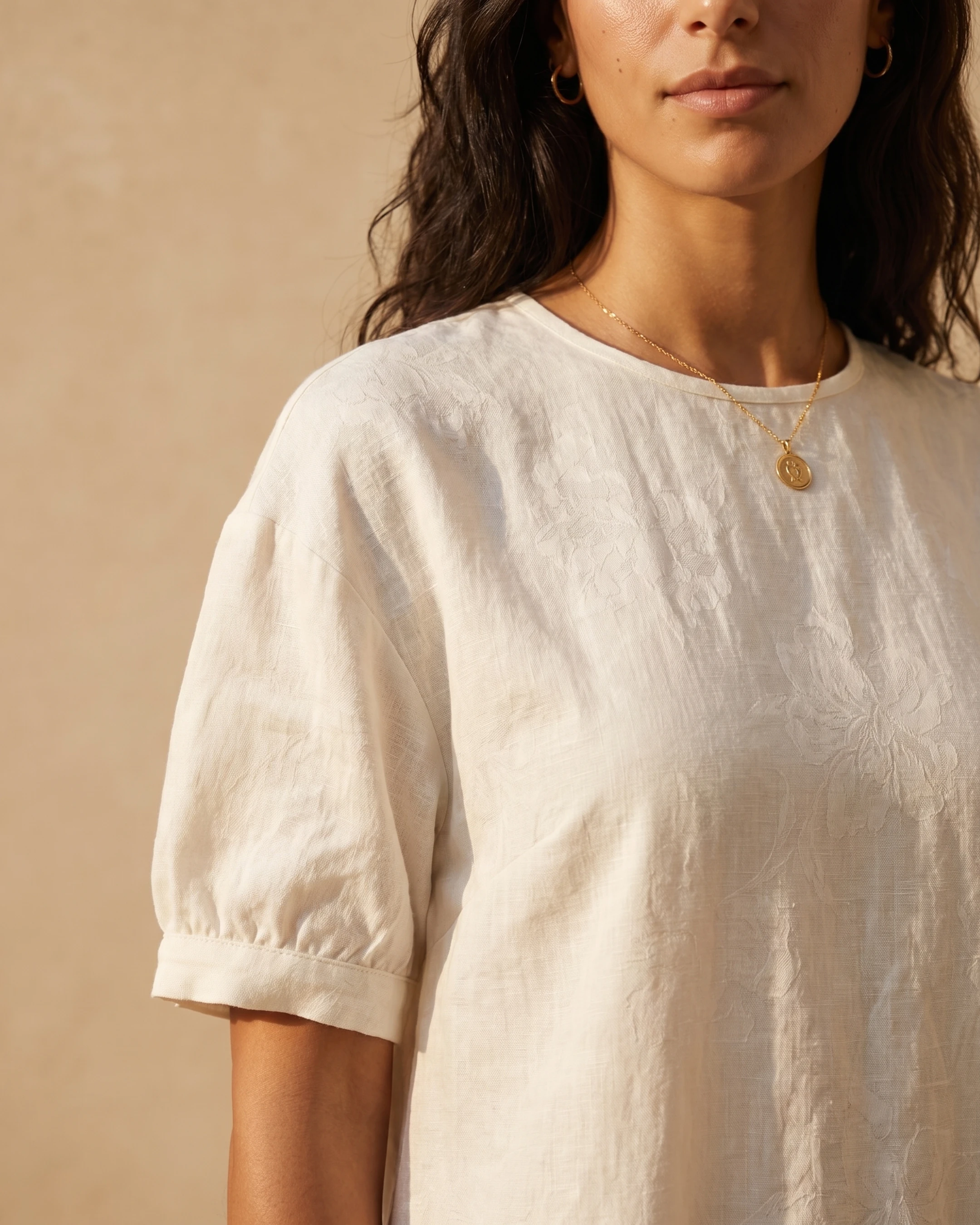 Detail of the Hugo Caesar Tassi Pomponia linen dress in Avorio, showing the round neckline, short gathered puff sleeve and tonal woven floral linen in a Roman travertine studio