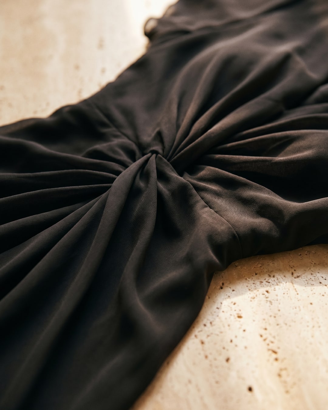 Macro of the Portia dress in Basalt — fluid charcoal chiffon and the centre twist-knot gather on warm travertine, Hugo Caesar Tassi