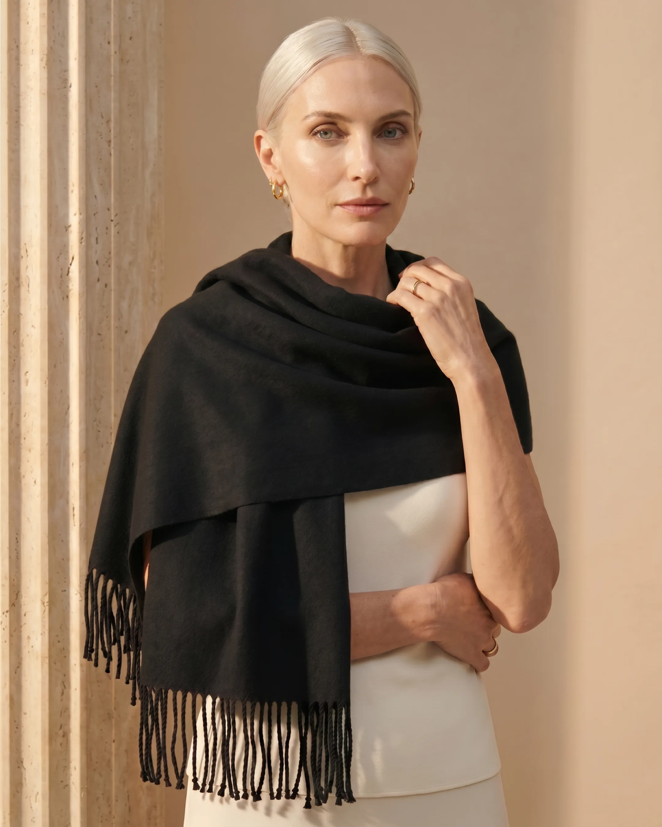 Hugo Caesar Tassi Ravenna fringed evening stole in Basalt worn around the shoulders in a warm travertine interior