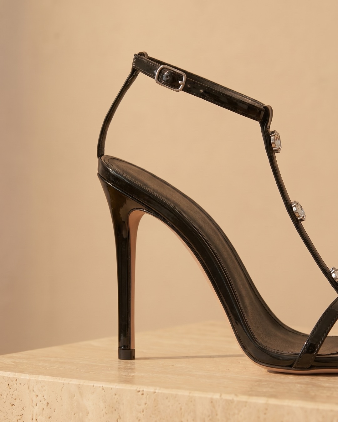 Hugo Caesar Tassi Sabella macro of the slim black patent stiletto heel, the fine T-bar and the clear crystal accents in claw settings
