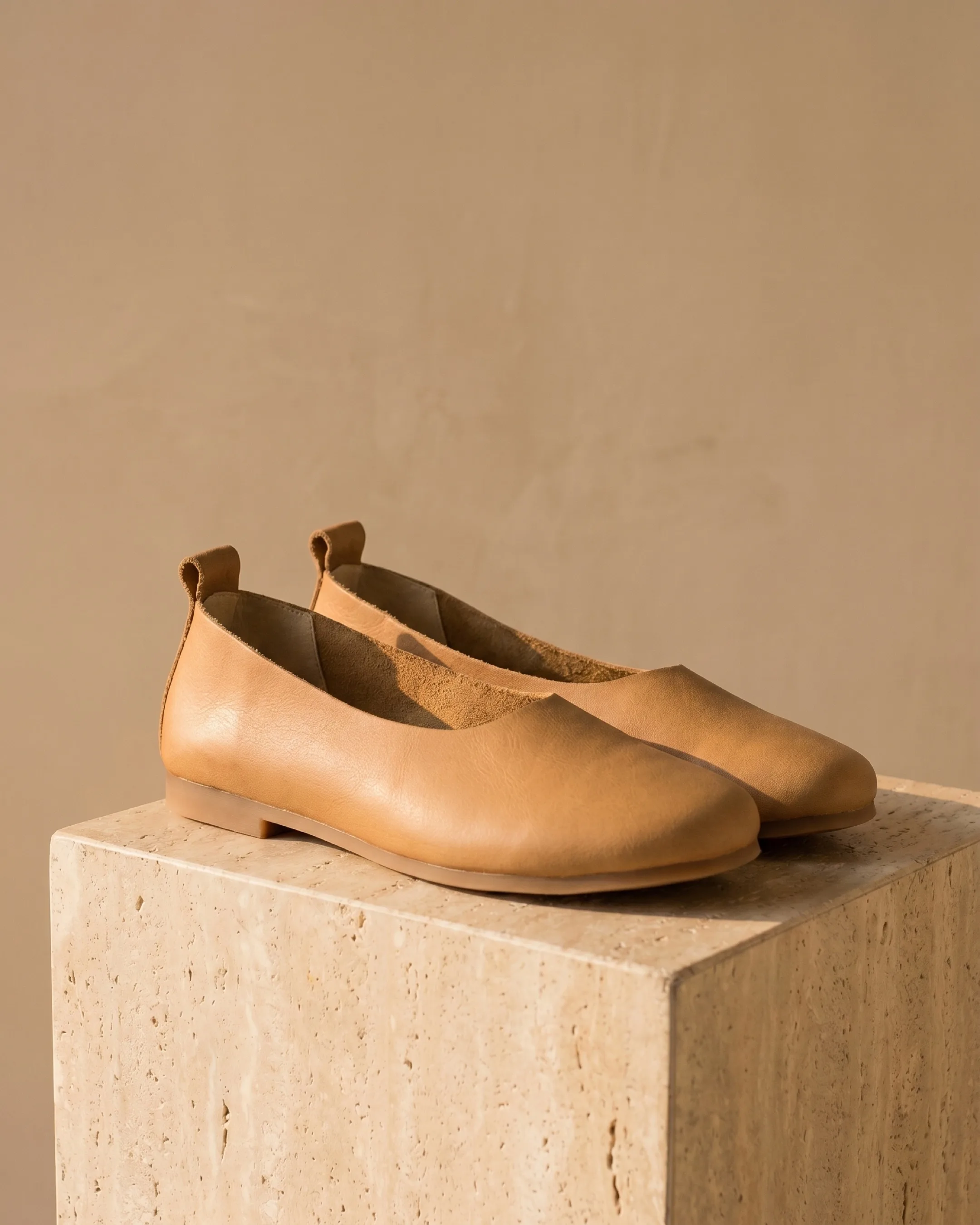 Hugo Caesar Tassi Septima soft cowhide slip-on ballet flats in Cuoio caramel leather, the pair on a warm travertine pedestal