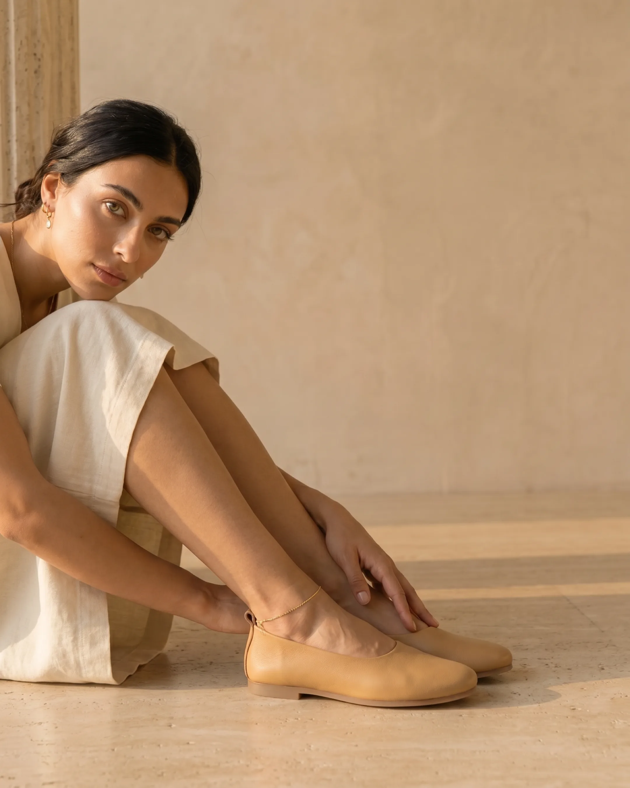 Hugo Caesar Tassi Septima caramel cowhide slip-on flats worn, an elegant cropped view of the lower legs beside a fluted travertine column