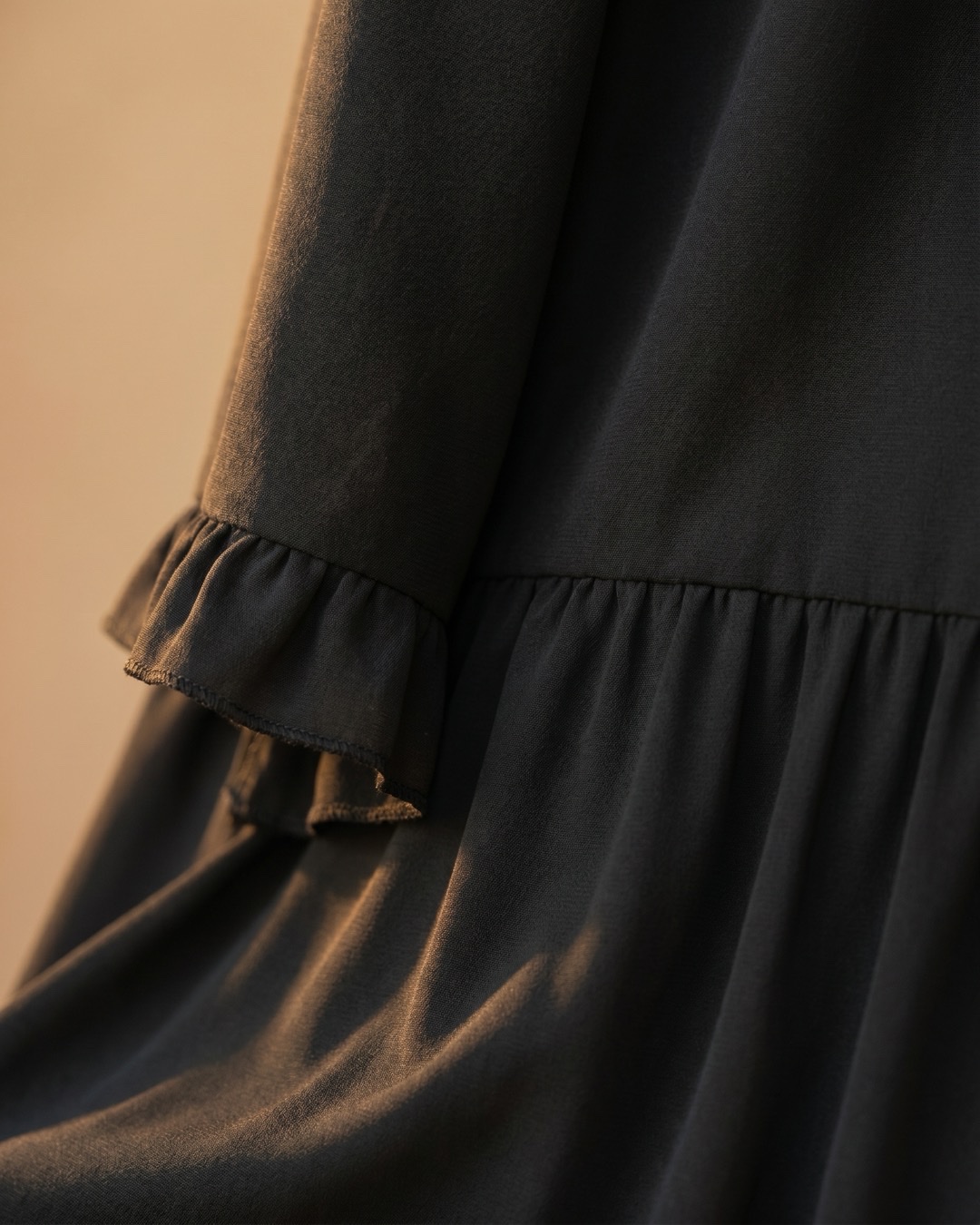Hugo Caesar Tassi Tertulla macro of soft matte black jersey-crepe knit showing the gathered tier seam and ruffled trim