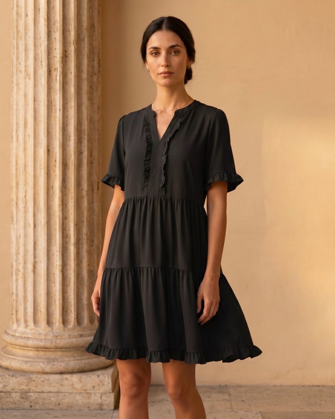 Hugo Caesar Tassi Tertulla black tiered swing dress beside a fluted travertine column in soft golden light
