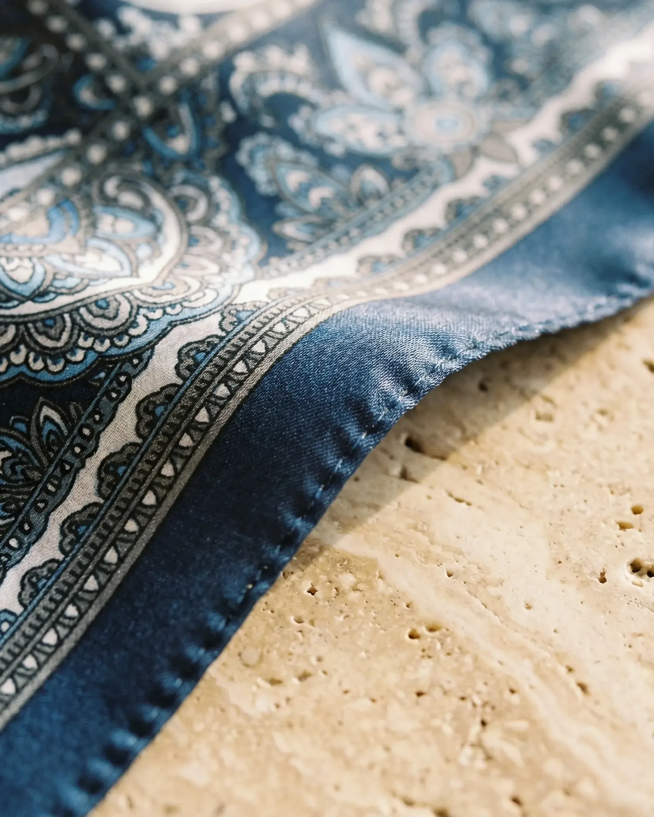 Macro detail of the Hugo Caesar Tassi Tessera scarf hand-rolled twill edge and silk-look satin weave in Cobalto navy on travertine