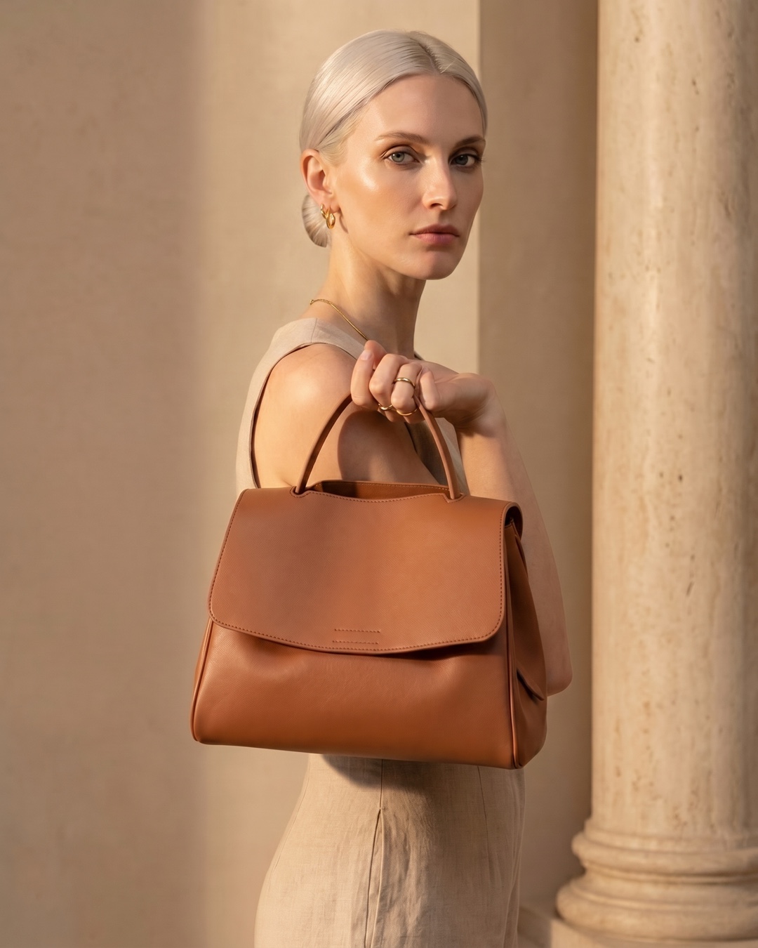 Hugo Caesar Tassi Tiberina cognac leather satchel carried by its arched top handle against a fluted travertine column