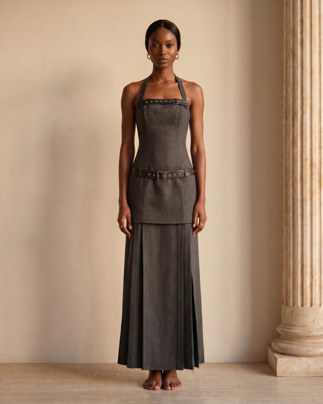 Hugo Caesar Tassi Verania studded-belt halter pleated column dress in Basalt charcoal, full-length front view against a travertine wall