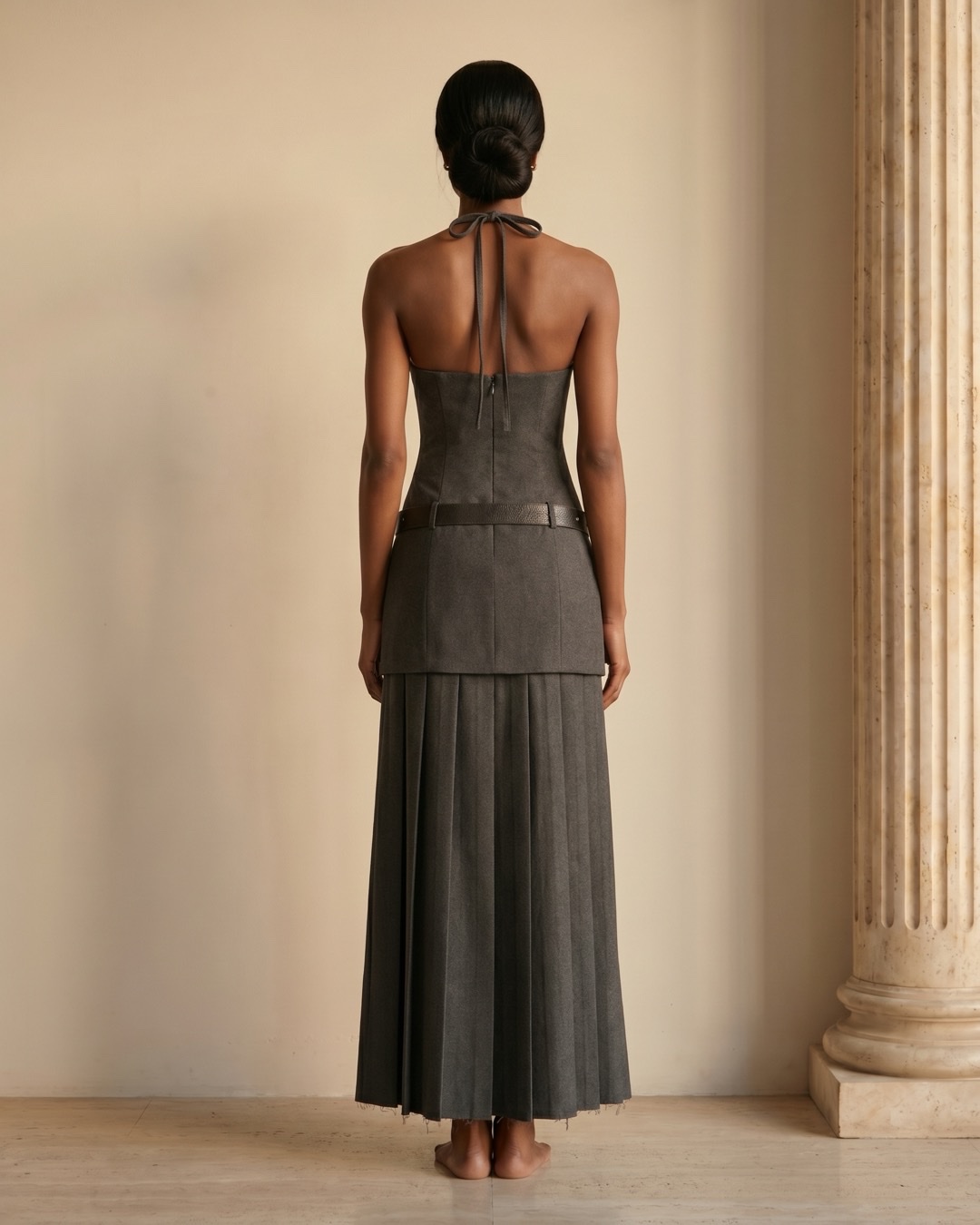 Hugo Caesar Tassi Verania full-length rear view showing the open halter back, centre-back zip, studded belt and long pleated skirt
